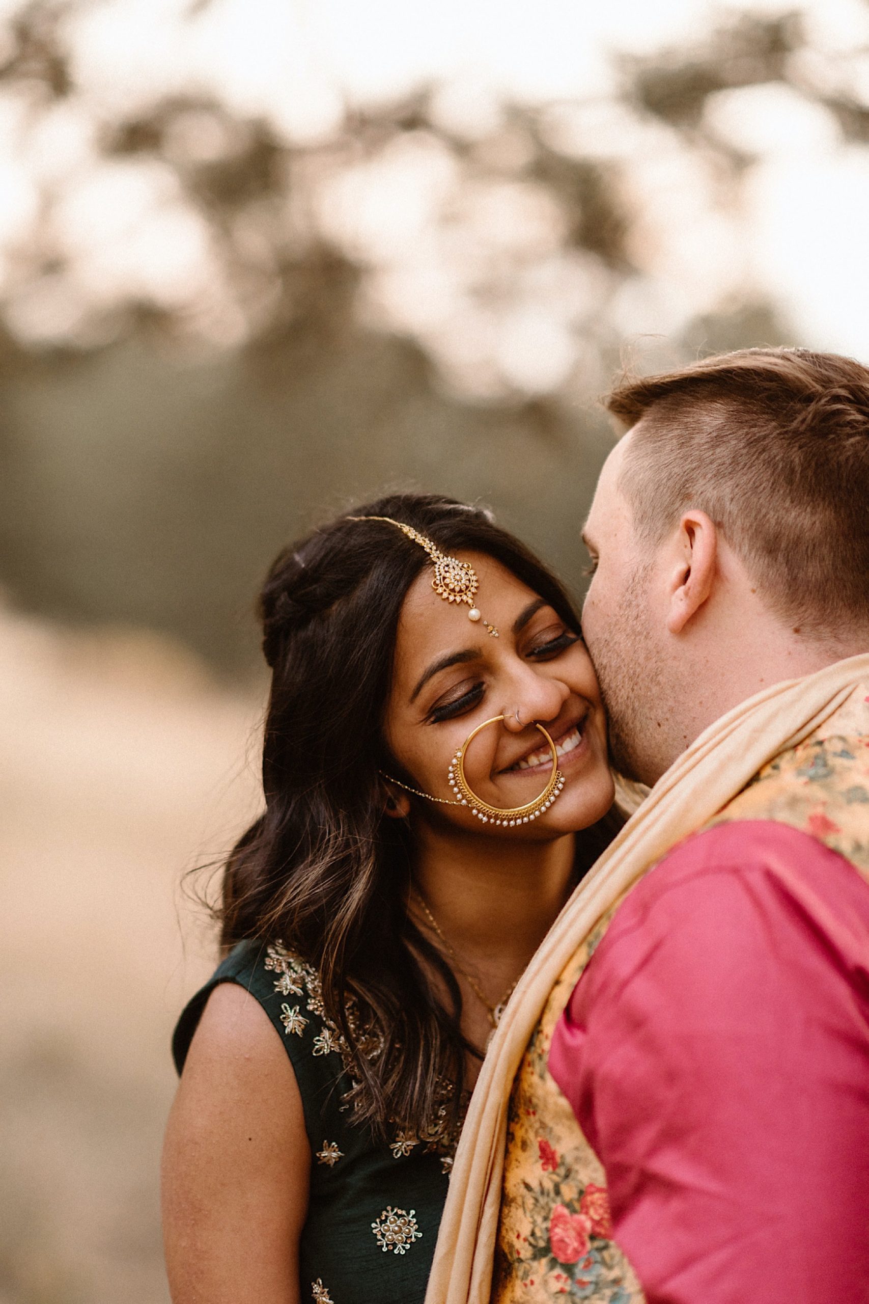 An Indian elopement couple stands in a field near Denver, Colorado as they snuggle up together. Photo by Denver elopement photographer, Colorado elopement photographer, Ashley Joyce Photography.