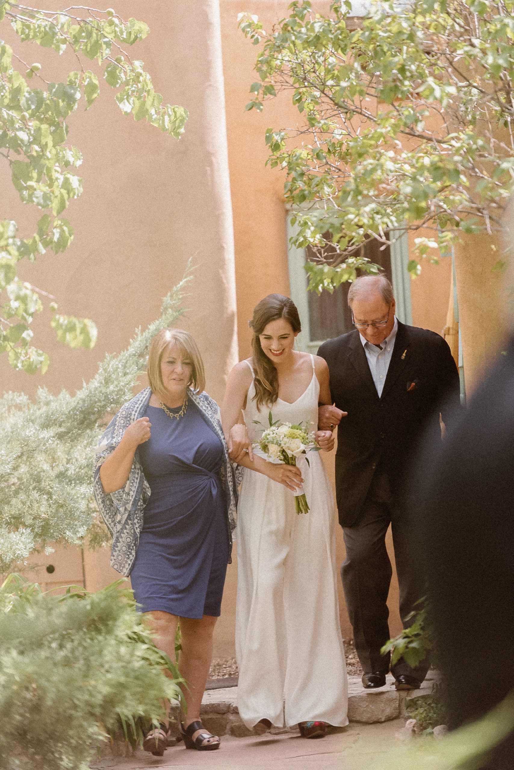 Bride walking down the aisle with her parents for her elopement | Santa Fe lesbian elopement photos at Inn of the Turquoise Bear in Santa Fe, New Mexico | Santa Fe lesbian elopement | Santa Fe elopement photographer | Santa Fe wedding | LGBTQ elopement | Photo by Denver Elopement Photographer Ashley Joyce Photography, copyright 2021