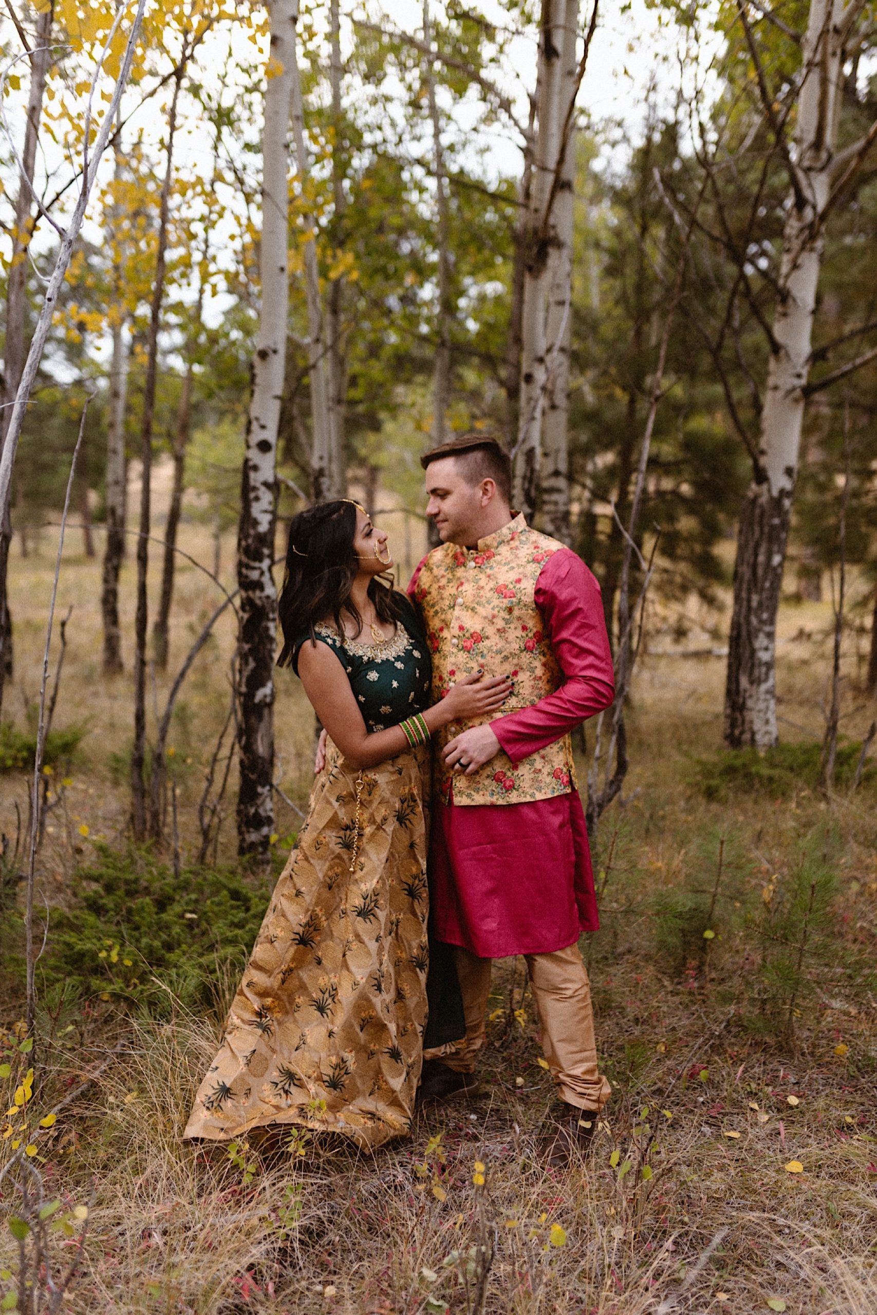An Indian wedding couple stands in a field of colorful aspens near Denver, Colorado as they snuggle up together for their Indian elopement photos. Photo by Denver elopement photographer, Colorado elopement photographer, Ashley Joyce Photography.