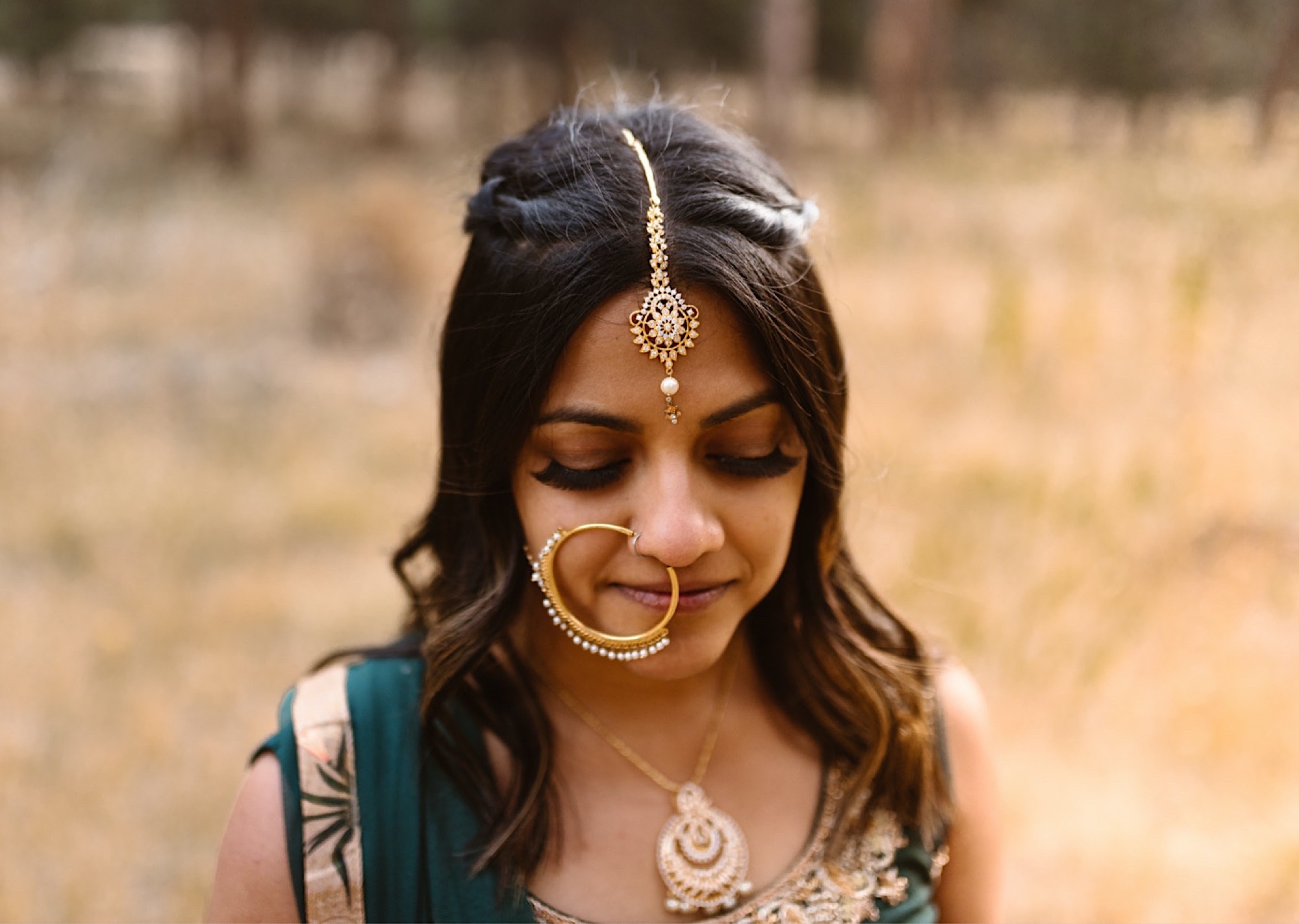 A Colorado Indian bride stands in her traditional Indian wedding attire for her elopement photos. The bride looks down as she displays her Indian wedding jewelry. Photo by Denver elopement photographer, Colorado elopement photographer, Ashley Joyce Photography.