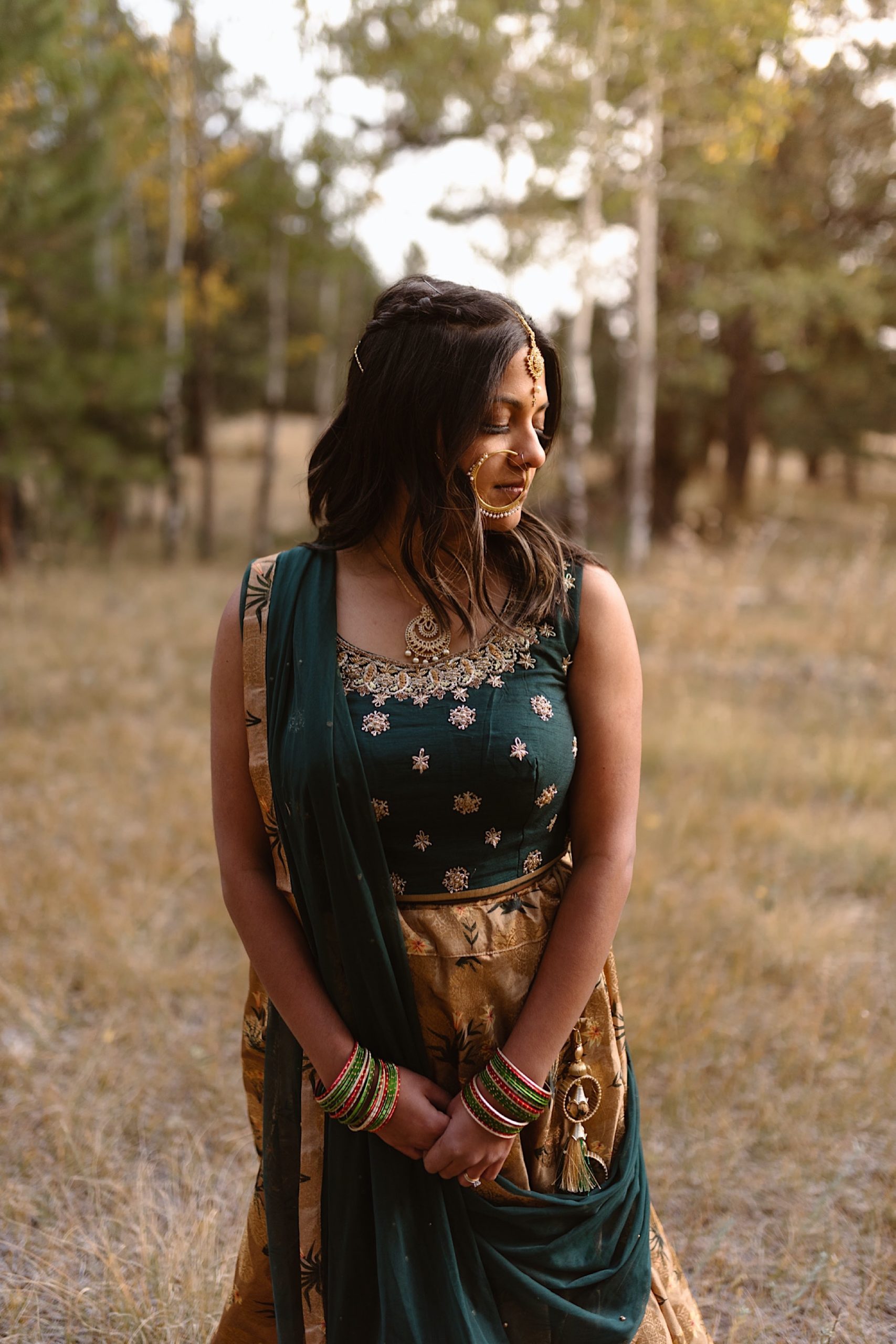 A Colorado Indian bride stands in her traditional Indian wedding attire for her elopement photos. The bride looks down and off to her left as she displays her Indian wedding jewelry and her Indian wedding attire. Photo by Denver elopement photographer, Colorado elopement photographer, Ashley Joyce Photography.
