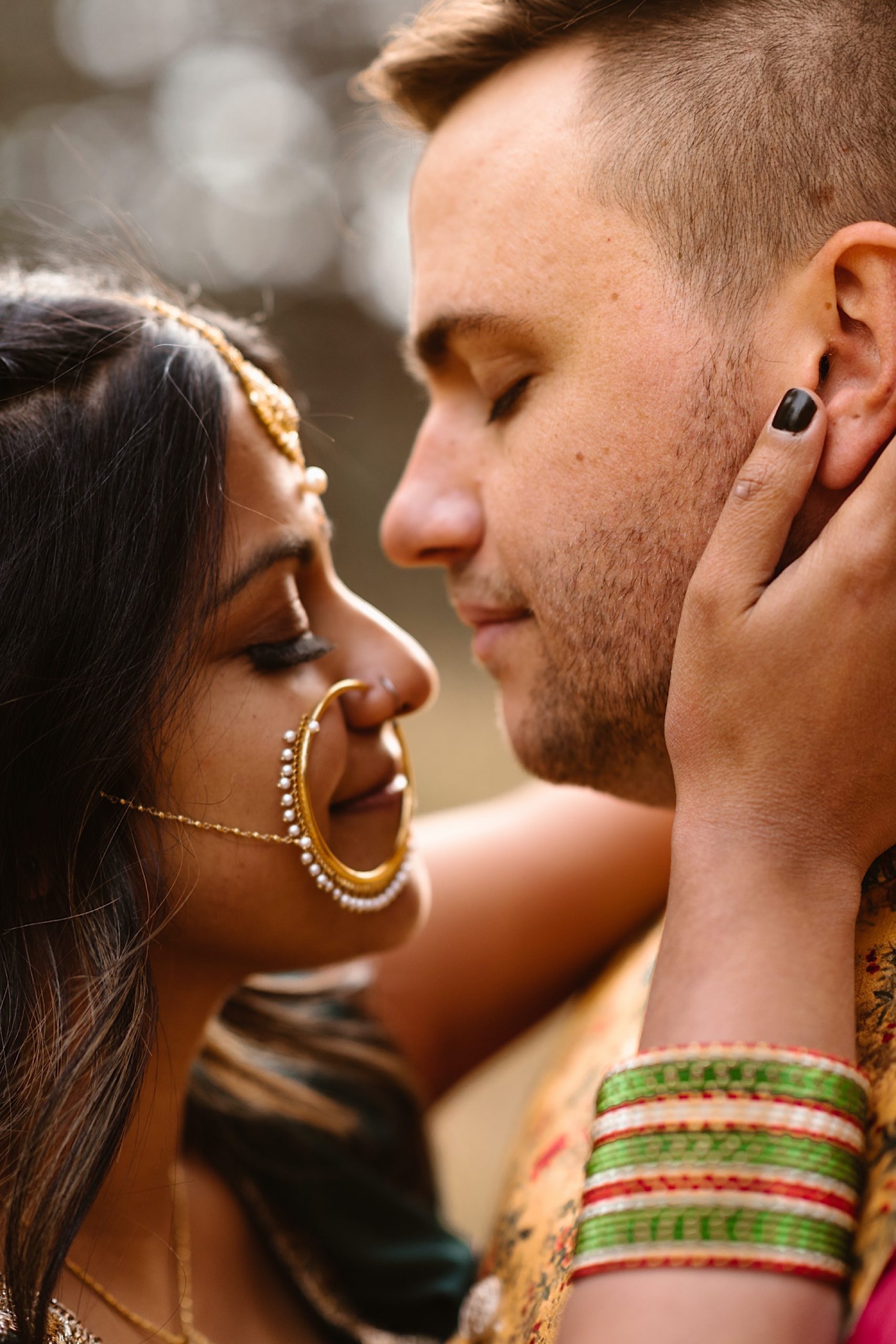 An Indian wedding couple stands in a field of evergreen trees near Denver, Colorado as the bride holds on to the groom’s face while they close their eyes. Photo by Denver elopement photographer, Colorado elopement photographer, Ashley Joyce Photography.