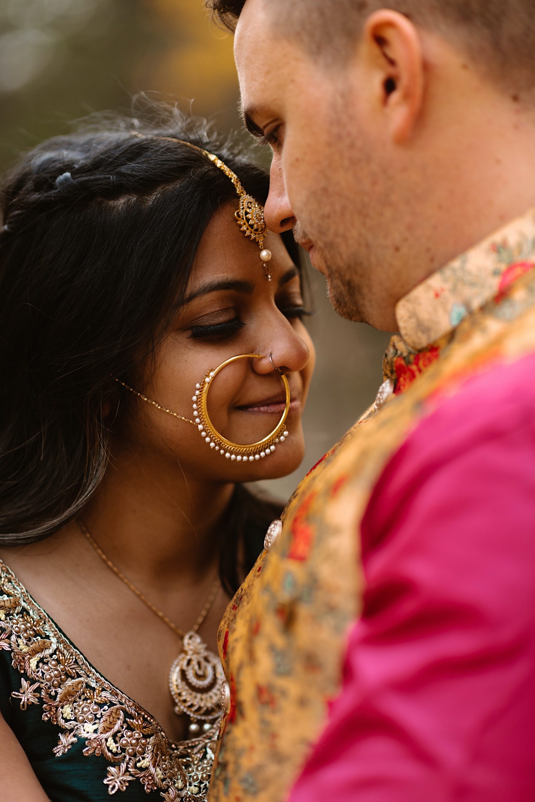 An Indian wedding couple stands in a field of evergreen trees near Denver, Colorado as the bride holds on to the groom’s face while they close their eyes. Photo by Denver elopement photographer, Colorado elopement photographer, Ashley Joyce Photography.