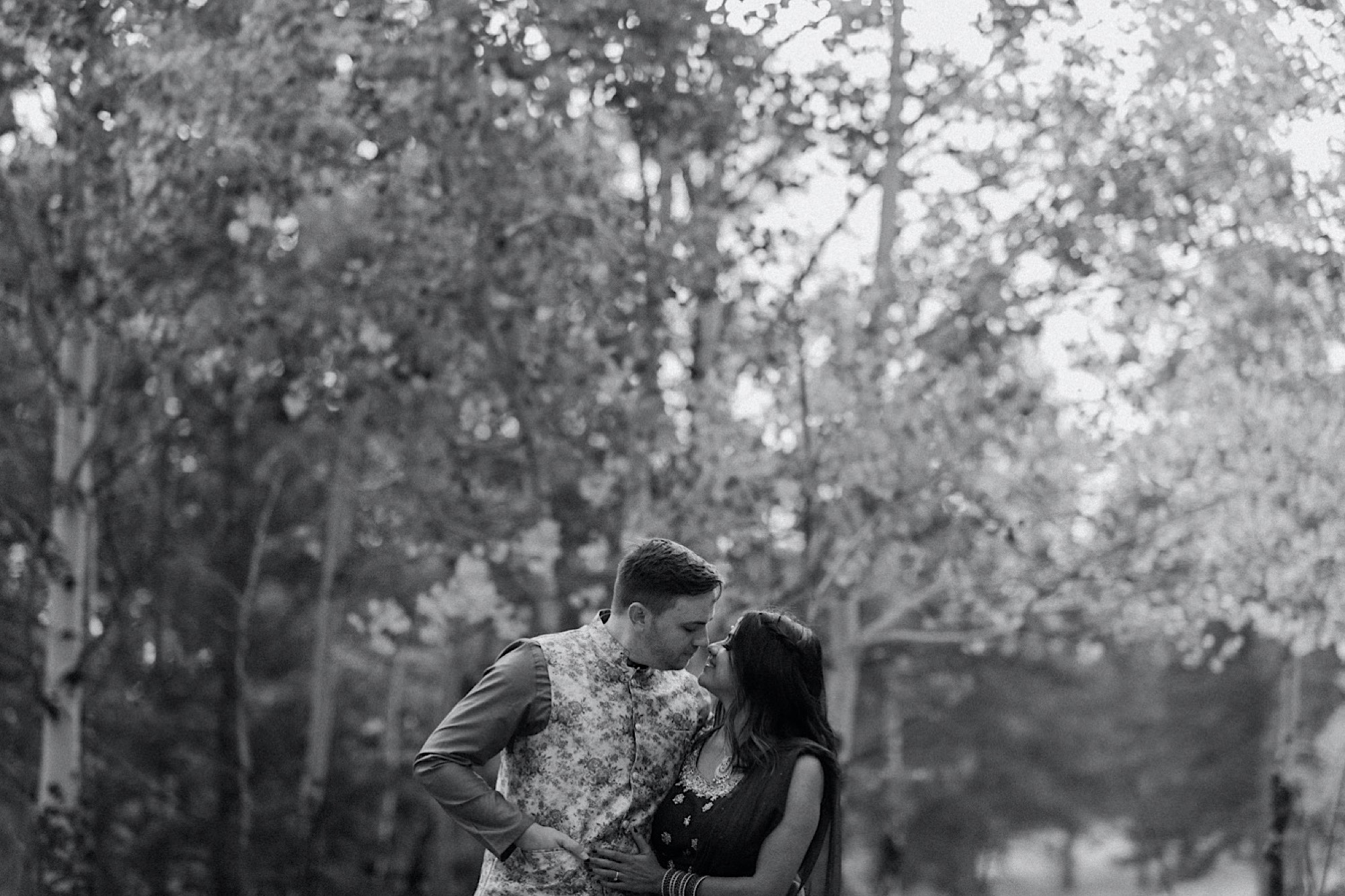 Black and white image of a Colorado Indian elopement couple as they stand in a field of aspen trees near Denver, Colorado as they snuggle up together for their Indian elopement photos. Photo by Denver elopement photographer, Colorado elopement photographer, Ashley Joyce Photography.