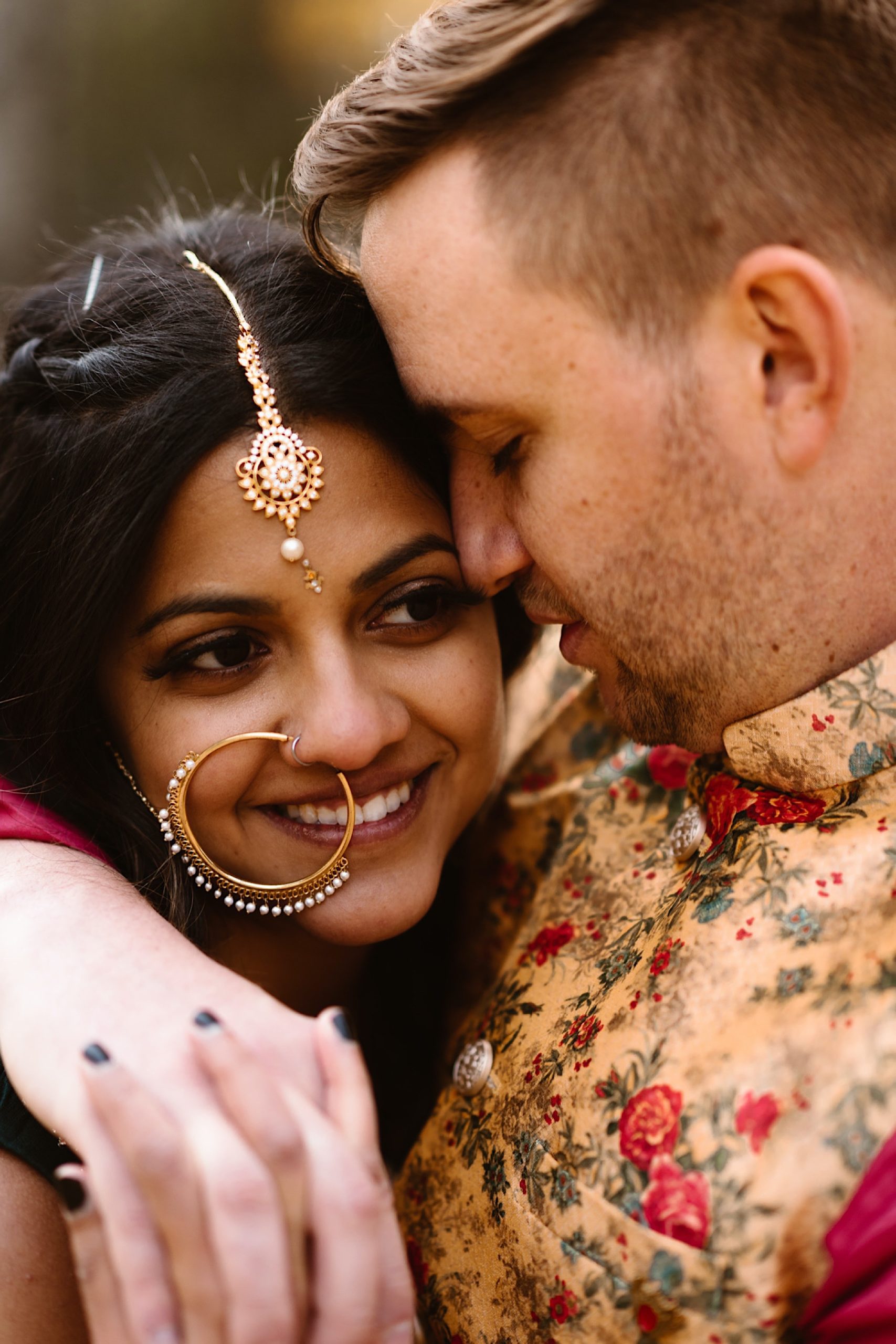 An Indian wedding couple stands in a field of evergreen trees near Denver, Colorado as the bride holds on to the groom’s face while they close their eyes. Photo by Denver elopement photographer, Colorado elopement photographer, Ashley Joyce Photography.