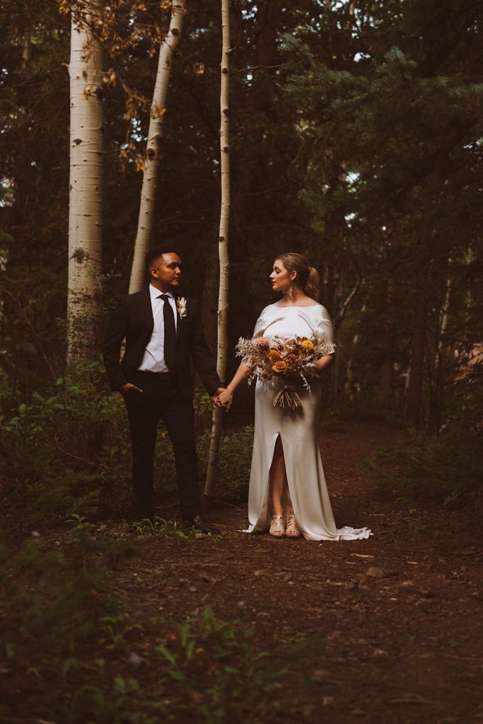 Bride and groom standing in the forest together holding hands in Colorado | Wedding portraits | Elopement portraits | Bride and groom elopement photos | Elopement wedding photos in Colorado | Colorado wedding photos | Colorado elopement photos | Elopement at Treehaus, Colorado | Treehaus Colorado | Colorado elopement | Treehaus elopement | Colorado elopement venue | Colorado mountain elopement venue | Unique elopement venue | Elopement venue in Colorado | Ashley Joyce Photography 2020