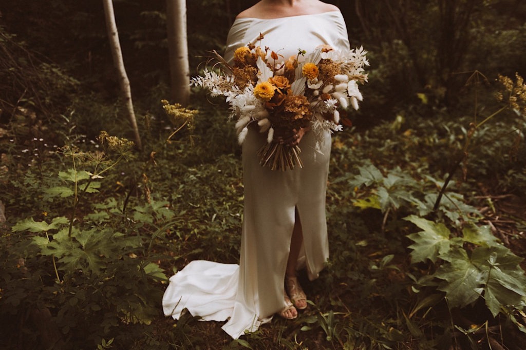 Bride standing in the woods of Colorado at Treehaus Colorado | Bride holding wedding bouquet | Wedding portraits | Elopement portraits | Bride and groom elopement photos | Elopement wedding photos in Colorado | Colorado wedding photos | Colorado elopement photos | Elopement at Treehaus, Colorado | Treehaus Colorado | Colorado elopement | Treehaus elopement | Colorado elopement venue | Colorado mountain elopement venue | Unique elopement venue | Elopement venue in Colorado | Ashley Joyce Photography 2020