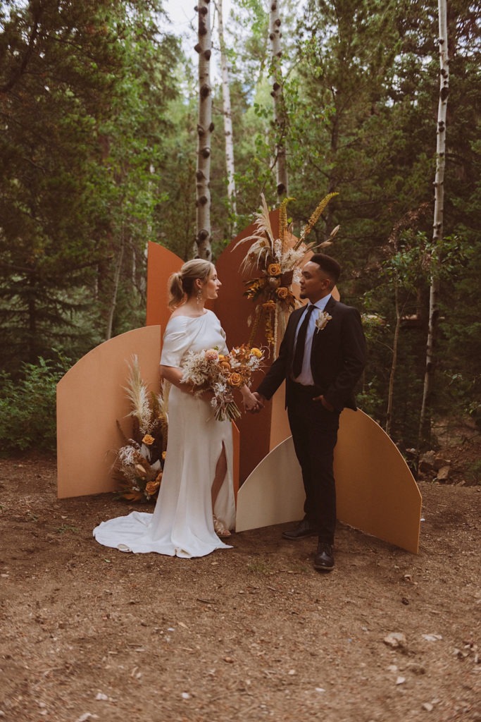 Bride and groom standing in front of a floral and wood arch in the forest | Floral arch detail | Elopement decor | Wedding decor | Wedding portraits | Elopement portraits | Bride and groom elopement photos | Elopement wedding photos in Colorado | Colorado wedding photos | Colorado elopement photos | Elopement at Treehaus, Colorado | Treehaus Colorado | Colorado elopement | Treehaus elopement | Colorado elopement venue | Colorado mountain elopement venue | Unique elopement venue | Elopement venue in Colorado | Ashley Joyce Photography 2020