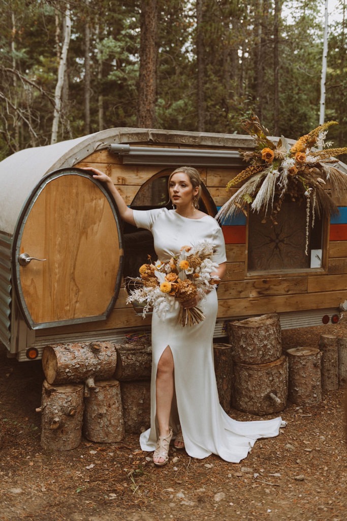 Bride standing with her bouquet in front of a teardrop trailer at Treehaus CO | Wedding portraits | Elopement portraits | Bride and groom elopement photos | Elopement wedding photos in Colorado | Colorado wedding photos | Colorado elopement photos | Elopement at Treehaus, Colorado | Treehaus Colorado | Colorado elopement | Treehaus elopement | Colorado elopement venue | Colorado mountain elopement venue | Unique elopement venue | Elopement venue in Colorado | Ashley Joyce Photography 2020
