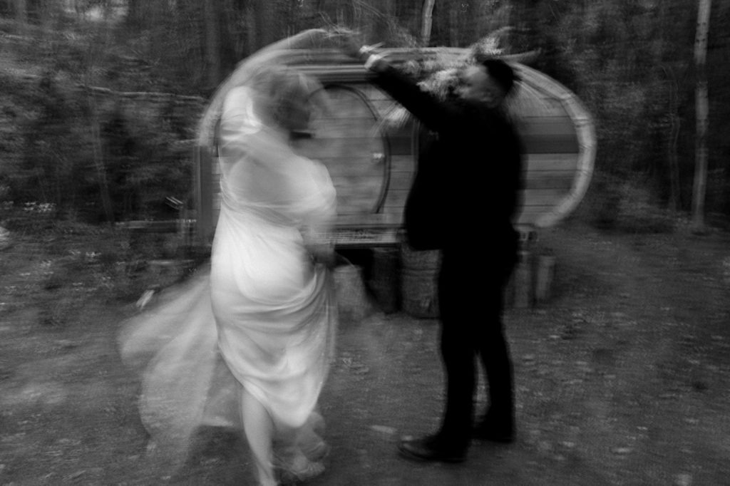 Black and white wedding photo of bride and groom dancing in slow motion in front of a teardrop trailer at Treehaus CO | Treehaus Colorado | Wedding portraits | Elopement portraits | Bride and groom elopement photos | Elopement wedding photos in Colorado | Colorado wedding photos | Colorado elopement photos | Elopement at Treehaus, Colorado | Treehaus Colorado | Colorado elopement | Treehaus elopement | Colorado elopement venue | Colorado mountain elopement venue | Unique elopement venue | Elopement venue in Colorado | Prea James Bridal | Prea James wedding dress | Lovely Bride Denver | Ashley Joyce Photography 2020