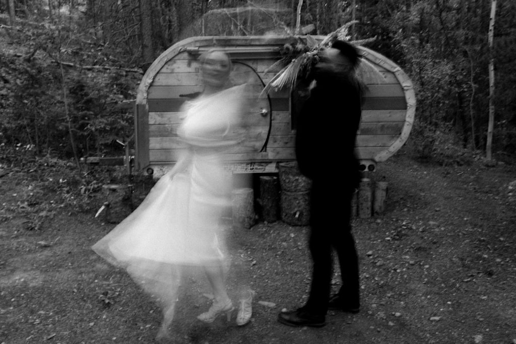 Black and white wedding photo of bride and groom dancing in slow motion in front of a teardrop trailer at Treehaus CO | Treehaus Colorado | Wedding portraits | Elopement portraits | Bride and groom elopement photos | Elopement wedding photos in Colorado | Colorado wedding photos | Colorado elopement photos | Elopement at Treehaus, Colorado | Treehaus Colorado | Colorado elopement | Treehaus elopement | Colorado elopement venue | Colorado mountain elopement venue | Unique elopement venue | Elopement venue in Colorado | Prea James Bridal | Prea James wedding dress | Lovely Bride Denver | Ashley Joyce Photography 2020