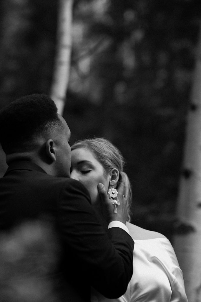 Black and white photo of groom kissing bride on the forehead | Wedding portraits | Elopement portraits | Bride and groom elopement photos | Elopement wedding photos in Colorado | Colorado wedding photos | Colorado elopement photos | Elopement at Treehaus, Colorado | Treehaus Colorado | Colorado elopement | Treehaus elopement | Colorado elopement venue | Colorado mountain elopement venue | Unique elopement venue | Elopement venue in Colorado | Prea James Bridal | Prea James wedding dress | Lovely Bride Denver | Ashley Joyce Photography 2020