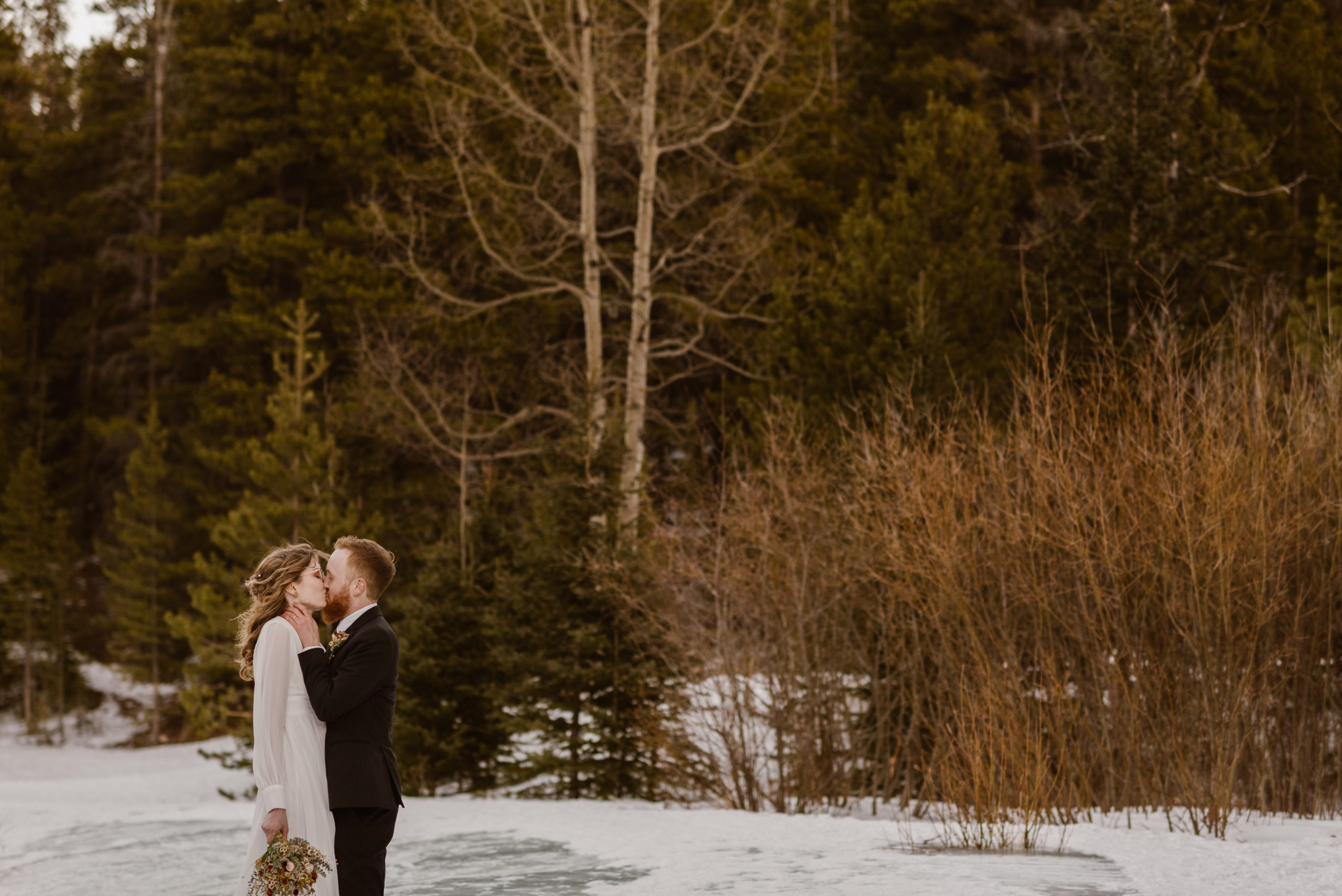 A Colorado elopement couple stands in the snow while they kiss after their intimate elopement near Morrison, Colorado. Photo by Denver elopement photographer, Colorado elopement photographer, Ashley Joyce Photography.