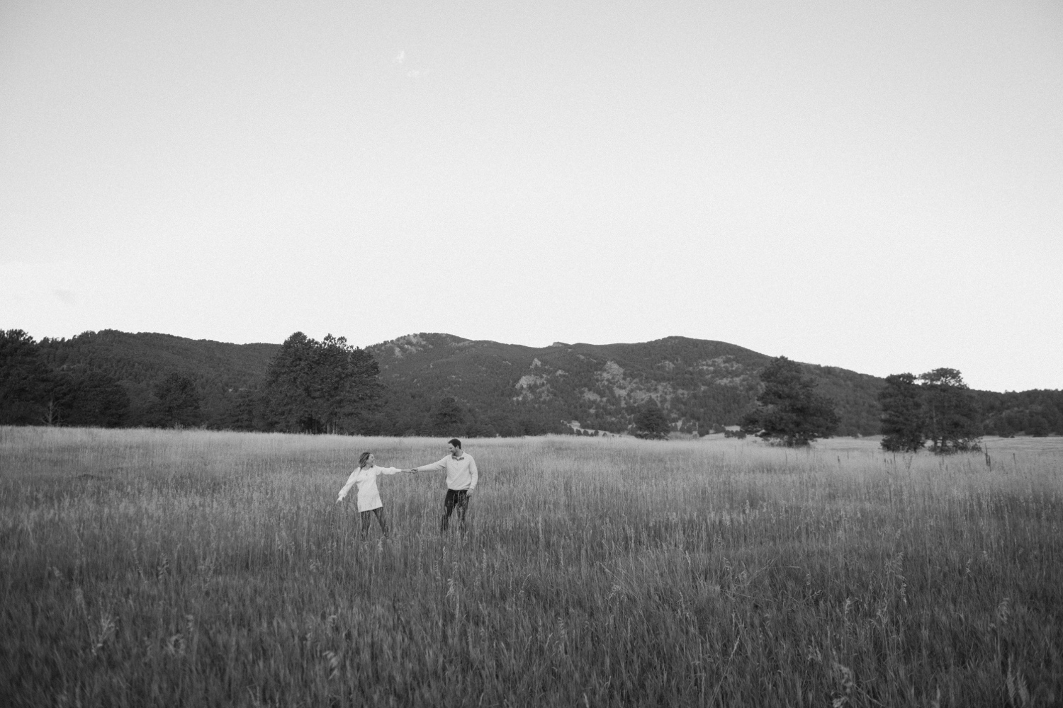 A black and white photo of an engaged couple walking through Elk Meadow Park in Evergreen, Colorado for their Colorado engagement photos, taken by Colorado wedding photographer Ashley Joyce Photography.
