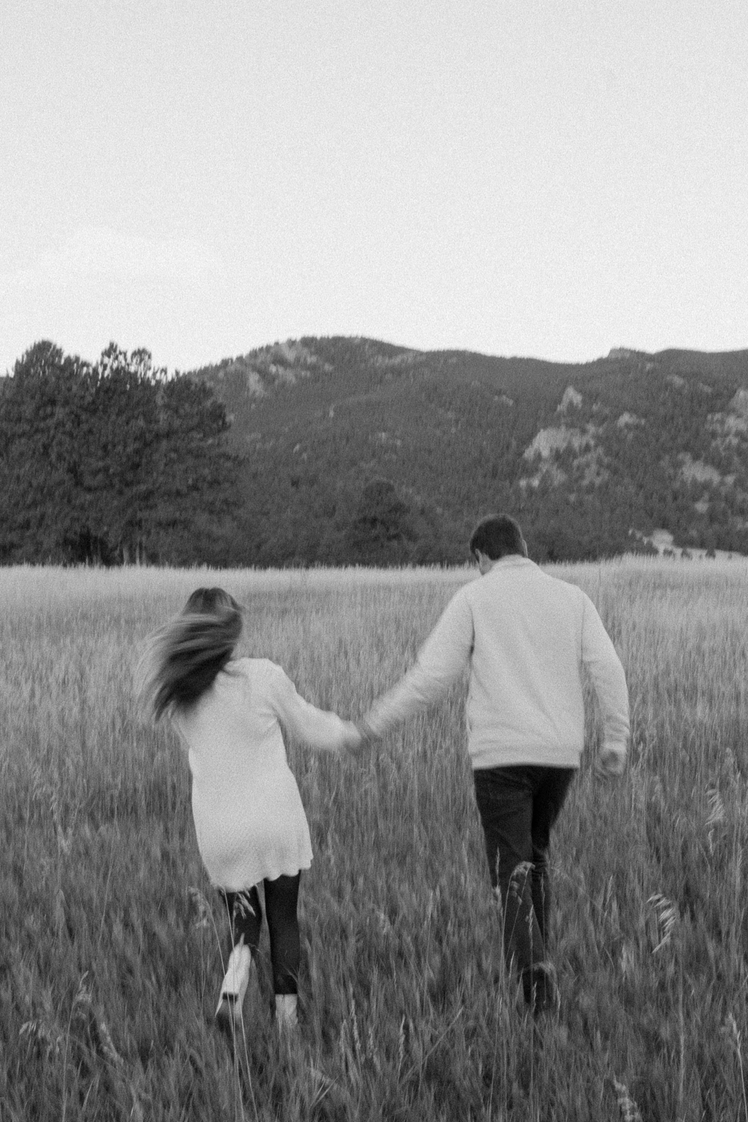 A black and white photo of an engaged couple walking through Elk Meadow Park in Evergreen, Colorado for their Colorado engagement photos, taken by Colorado wedding photographer Ashley Joyce Photography.