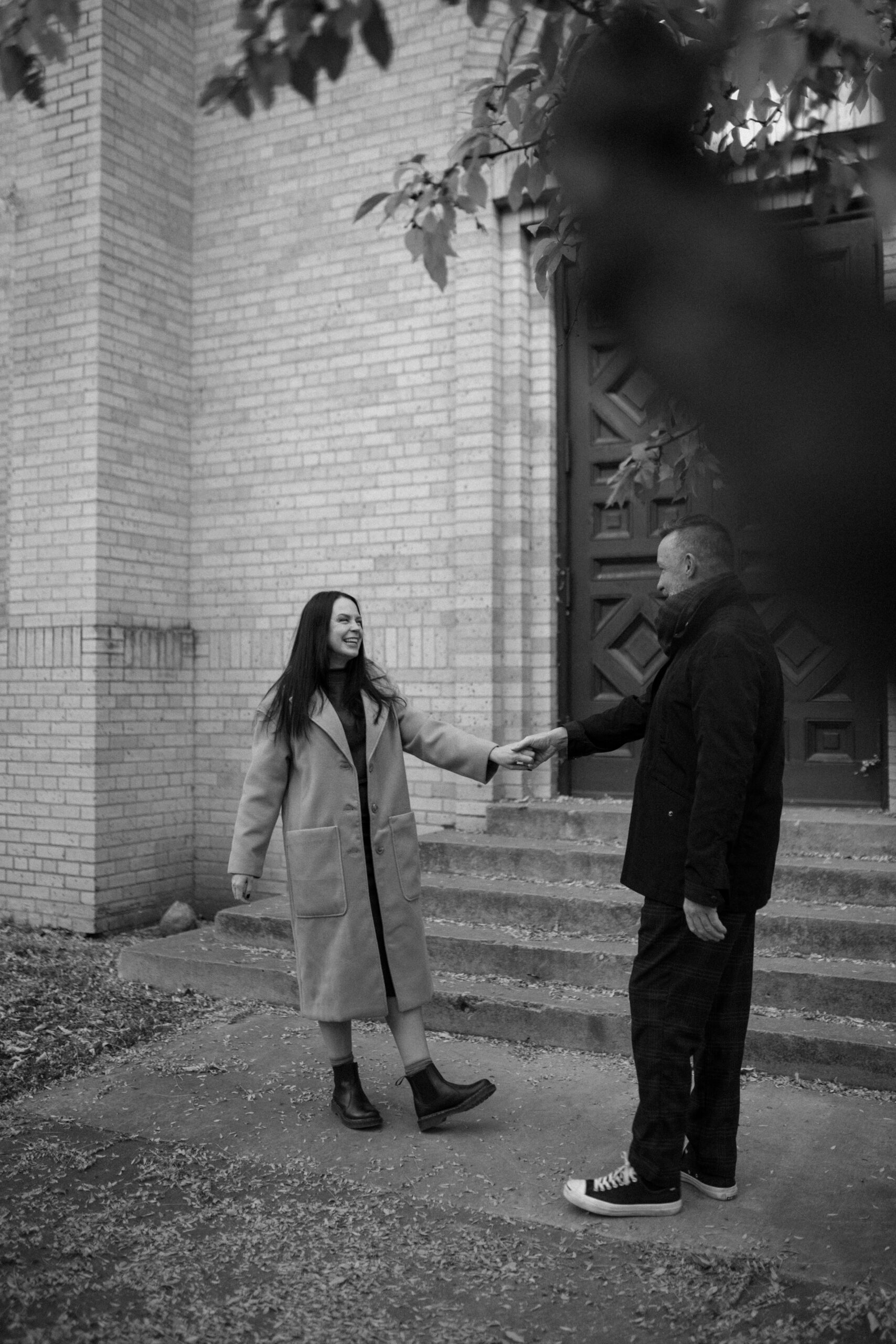 A black and white photo of an engaged couple holding hands in front of The Smiley Building in Durango, Colorado for their engagement session, taken by Colorado wedding photographer, Ashley Joyce.
