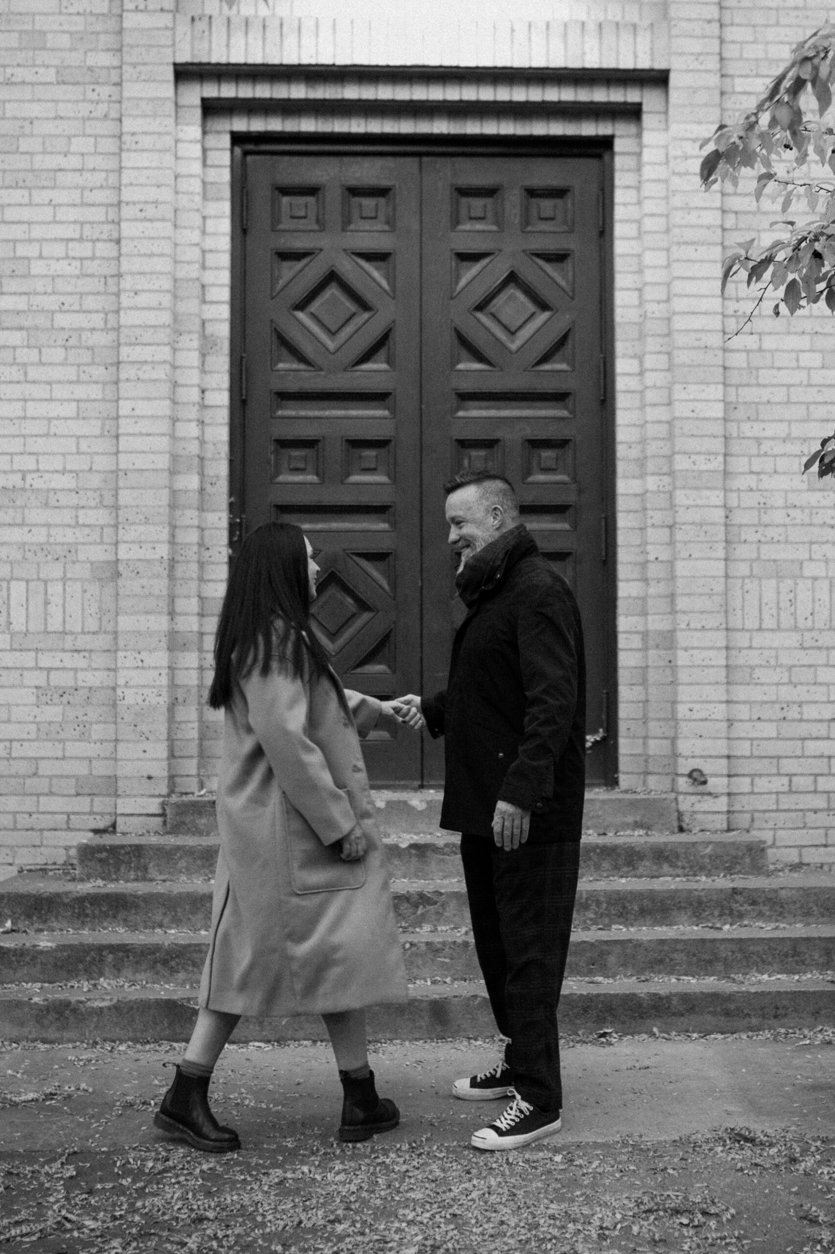 A black and white photo of an engaged couple dancing with one another in front of The Smiley Building in Durango, Colorado for their Durango engagement session, taken by Colorado wedding photographer, Ashley Joyce.