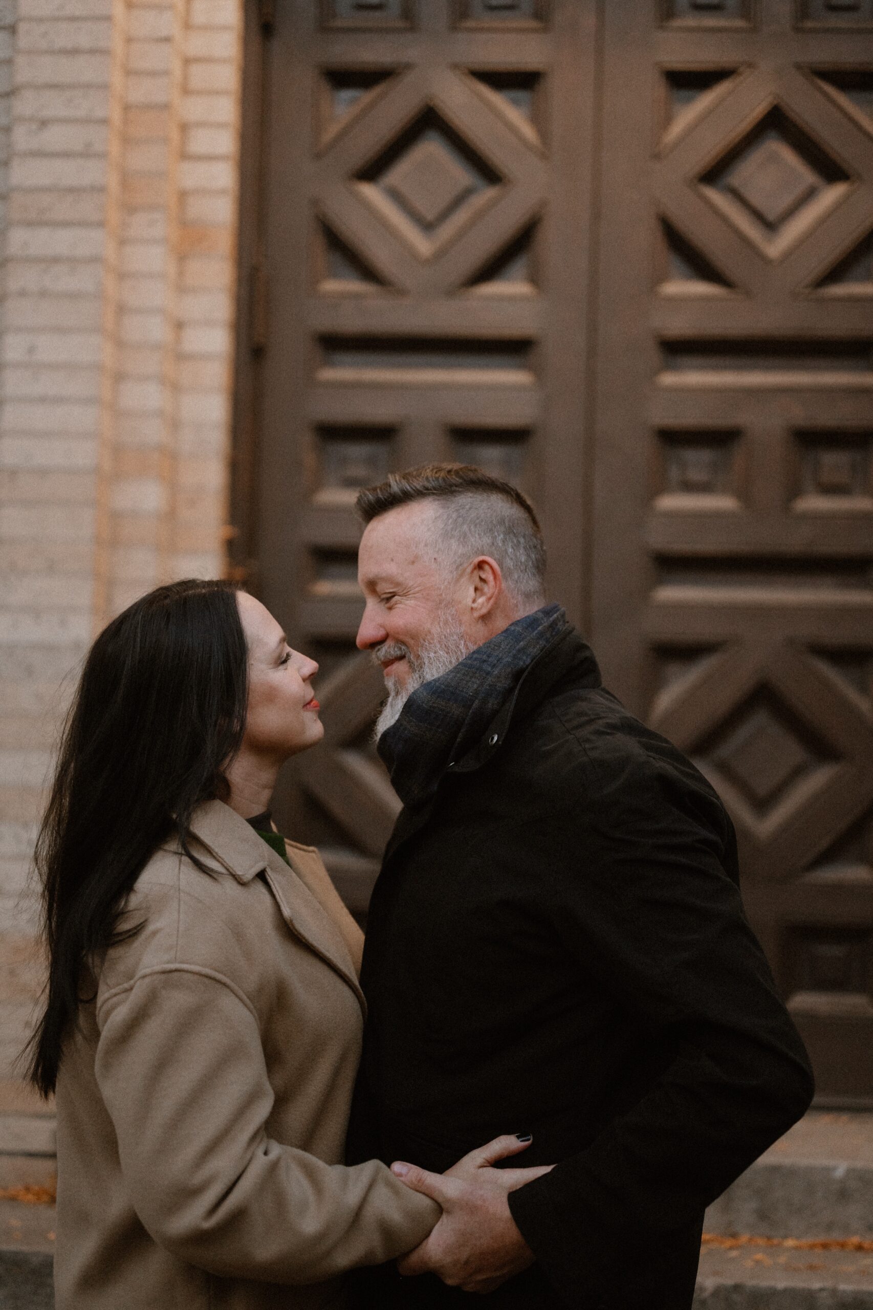 A color photo of an engaged couple embracing one another while they gaze into each other’s eyes in front of the Smiley Building for their Durango engagement session. Photo by Colorado wedding photographer Ashley Joyce.