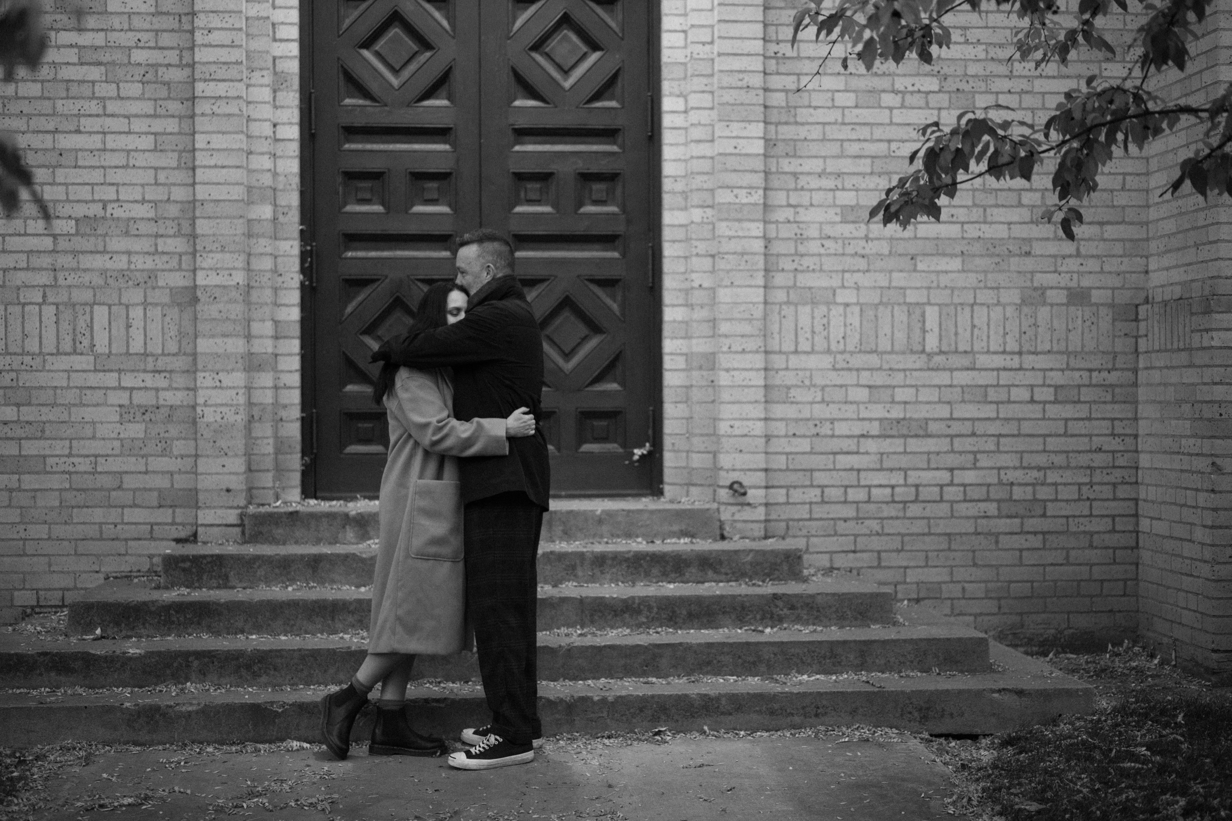 A black and white photo of an engaged couple embracing one another in front of The Smiley Building in Durango, Colorado for their engagement session, taken by Colorado wedding photographer, Ashley Joyce.