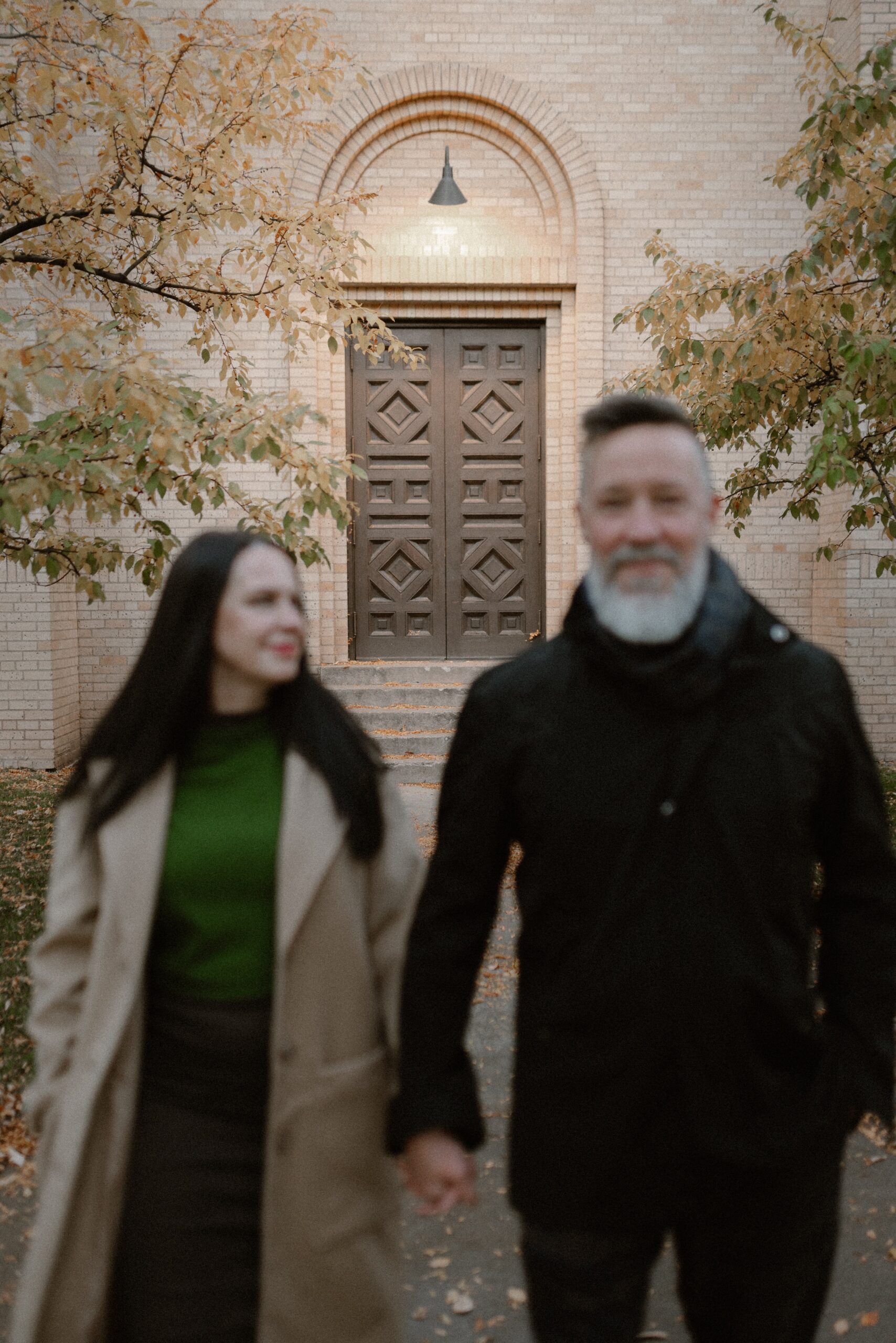 A blurry color photo of an engaged couple holding hands in front of The Smiley Building in Durango, Colorado during the fall for their engagement session, taken by Colorado wedding photographer, Ashley Joyce.