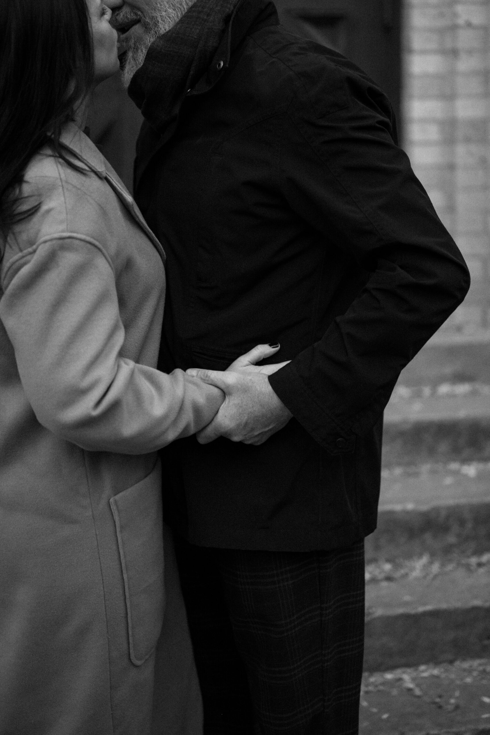 A black and white photo of an engaged couple embracing and kissing one another in front of The Smiley Building in Durango, Colorado for their engagement session, taken by Colorado wedding photographer, Ashley Joyce.