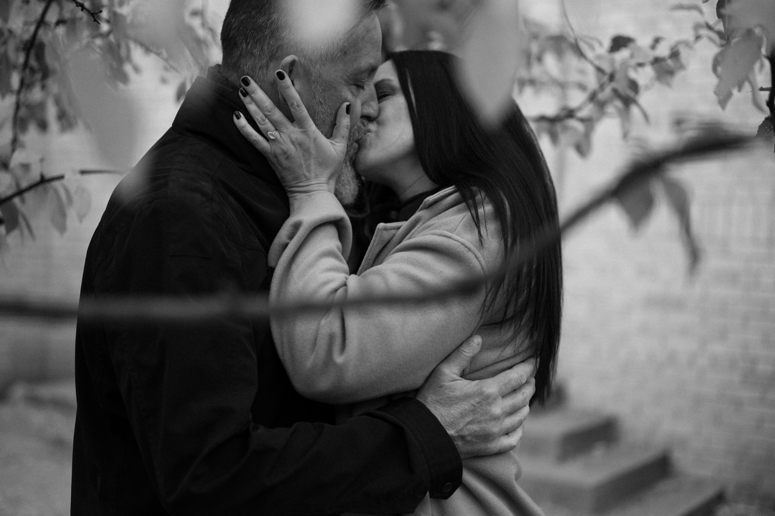 A black and white photo of an engaged couple kissing one another in front of The Smiley Building in Durango, Colorado for their engagement session, taken by Colorado wedding photographer, Ashley Joyce.