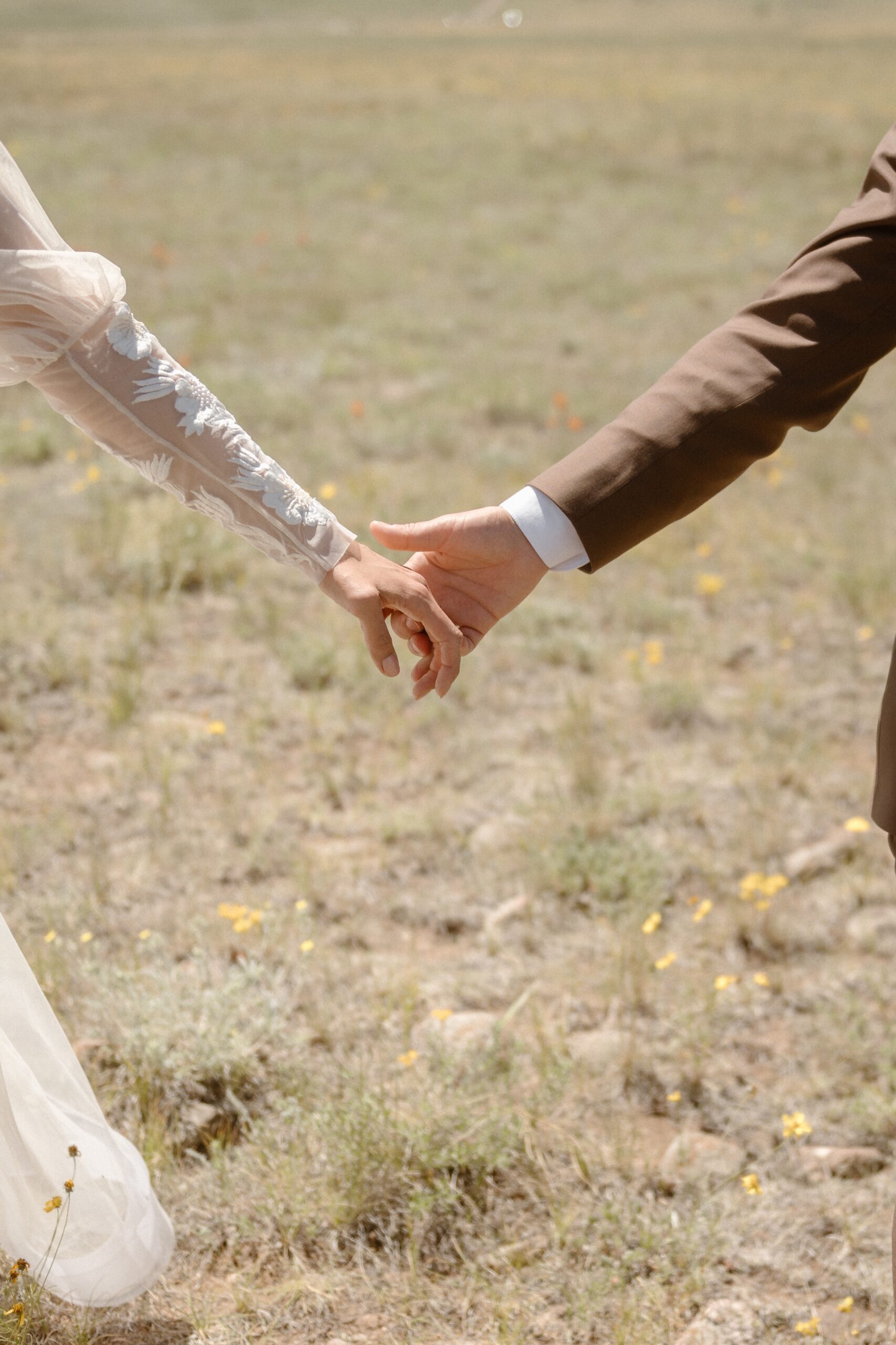 A closeup of a couple holding hands in a grassy field. Photo by Colorado wedding photographer Ashley Joyce.