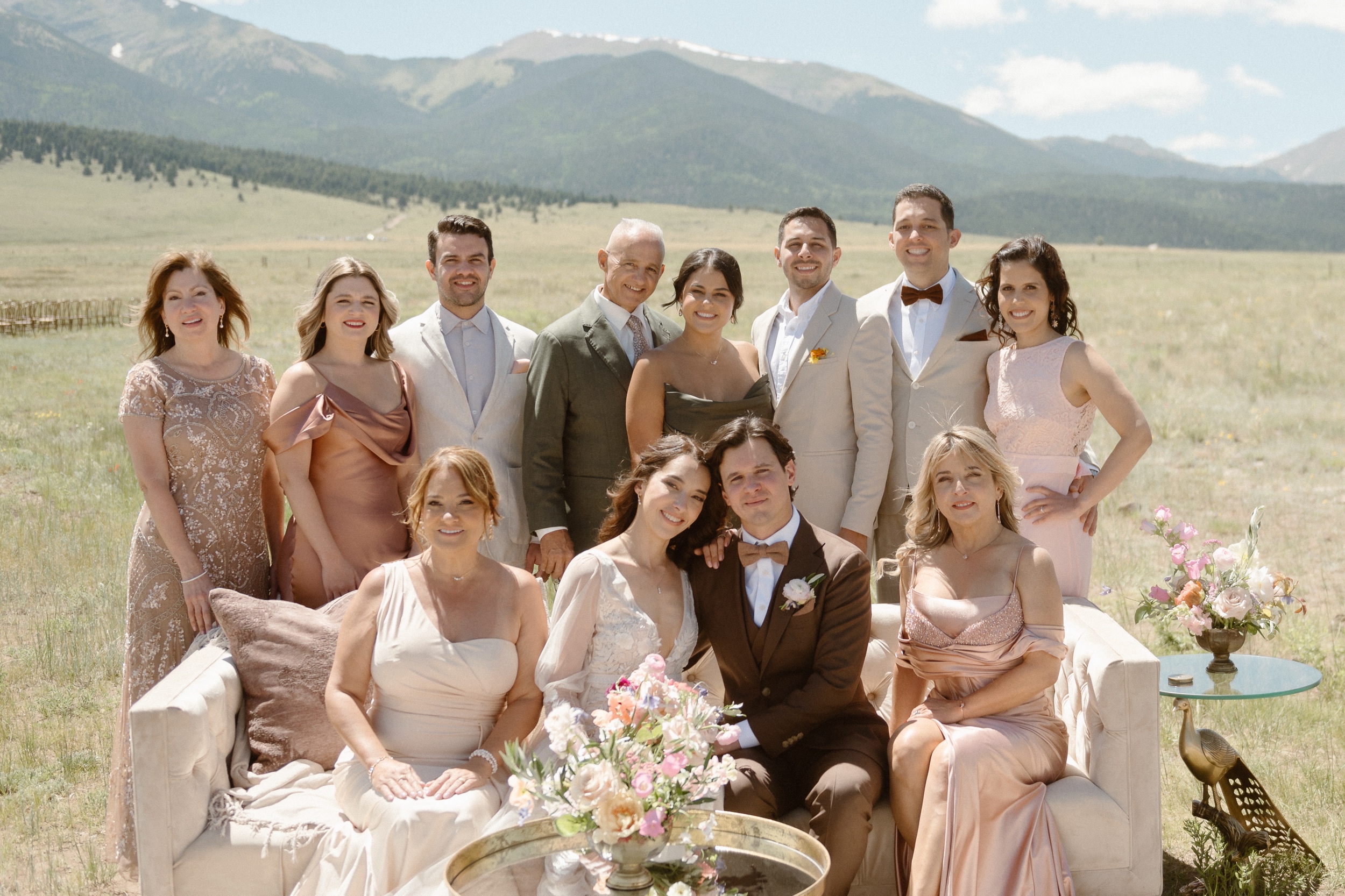 A group photo of a bride and groom's immediate families while they pose in a grassy field with mountains in the background. Photo by Colorado wedding photographer Ashley Joyce.