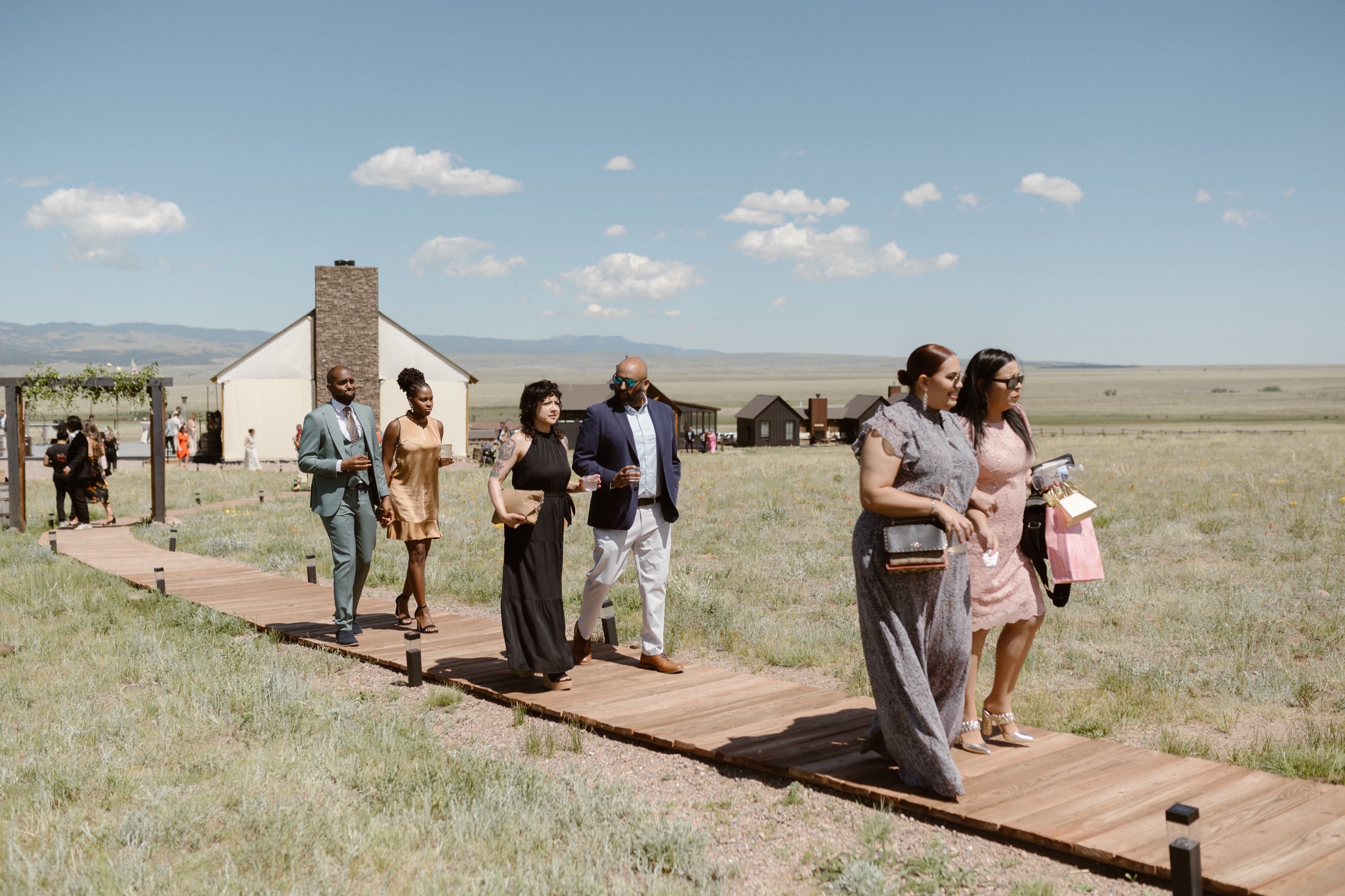 Wedding guests walking along a wooden path to find their seats for the wedding ceremony at Three Peaks Ranch. Photo by Colorado wedding photographer Ashley Joyce.