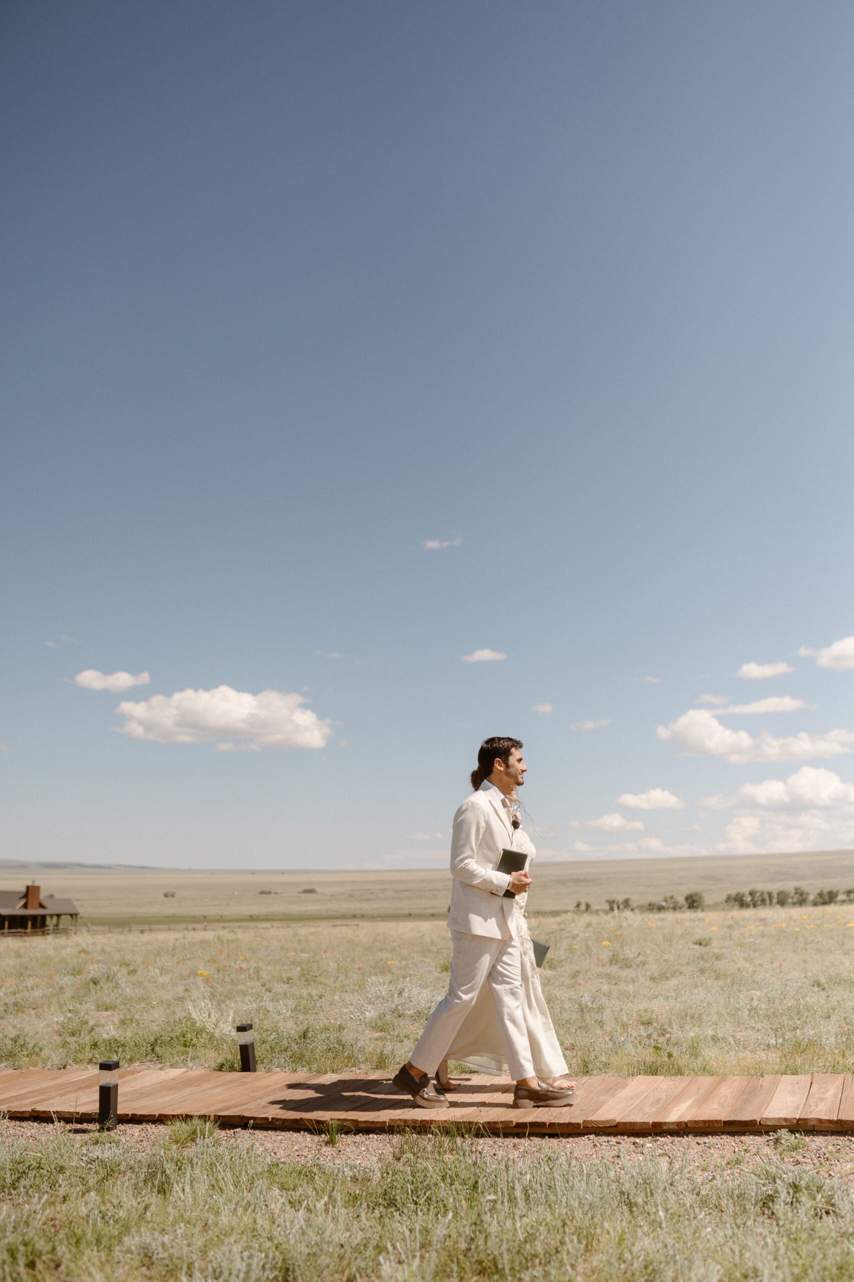 Two officiants walk along a wooden path to the wedding ceremony site at Three Peaks Ranch. Photo by Colorado wedding photographer, Ashley Joyce