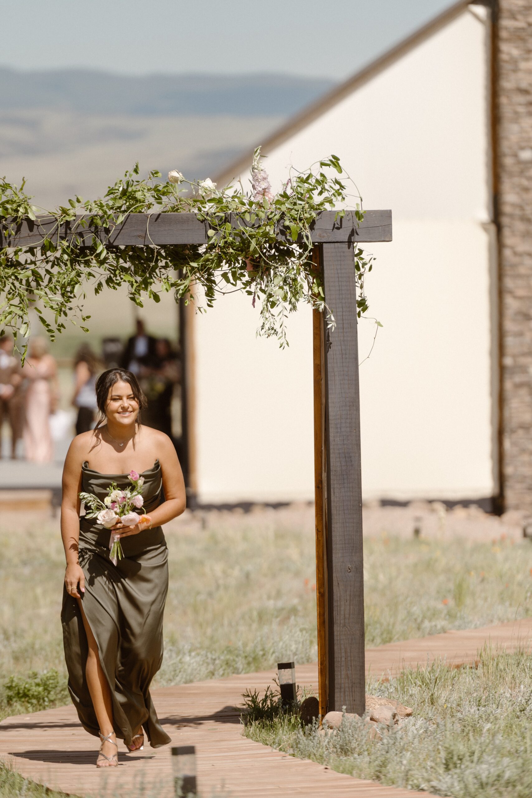 A bridesmaid walks along a wooden path to the wedding ceremony location at Three Peaks Ranch. Photo by Colorado wedding photographer Ashley Joyce.