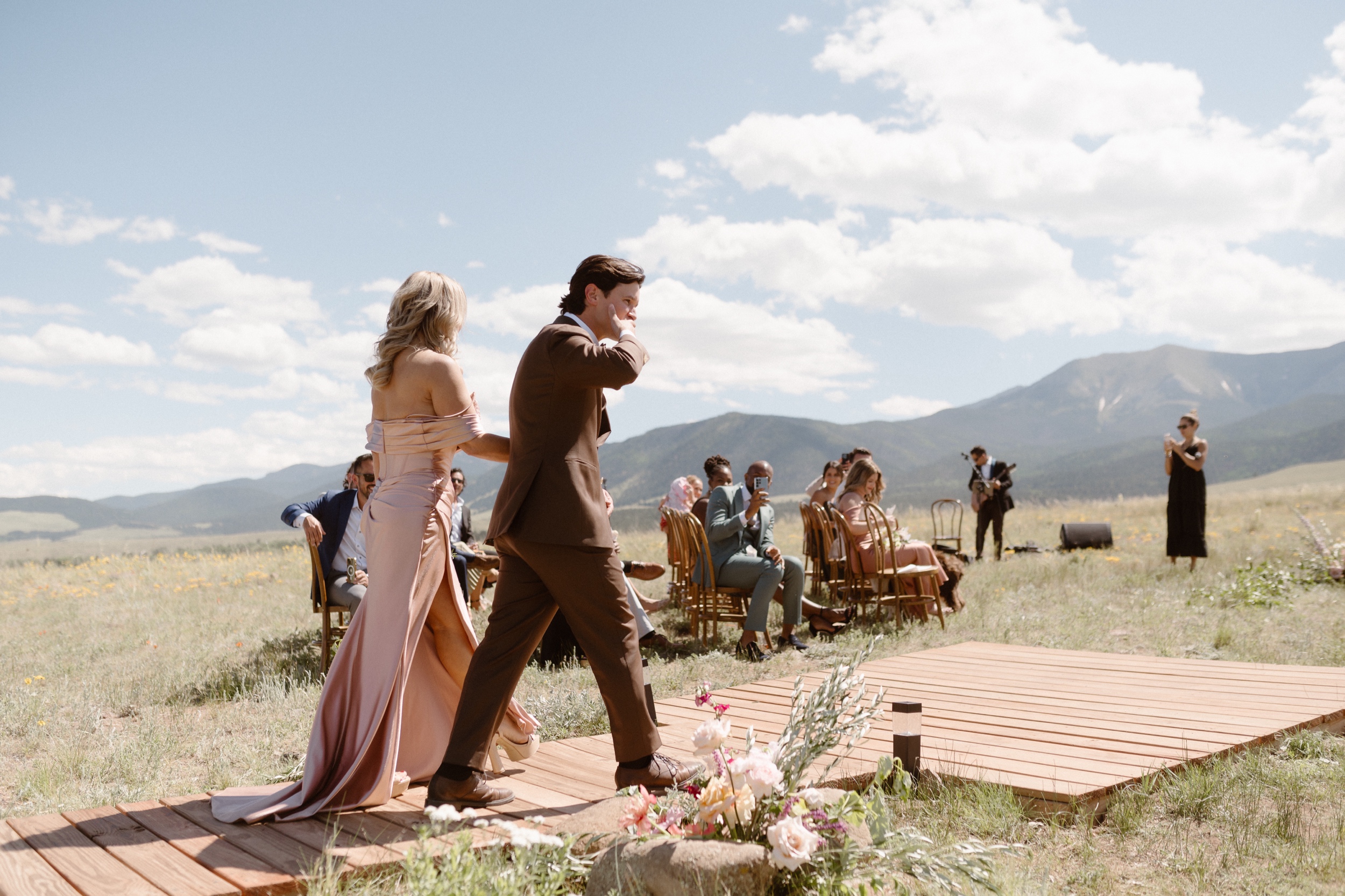 A groom and his mom walk along a wooden path to the ceremony location as he gets ready for his Three Peaks Ranch Wedding. Photo by Colorado wedding photographer Ashley Joyce.