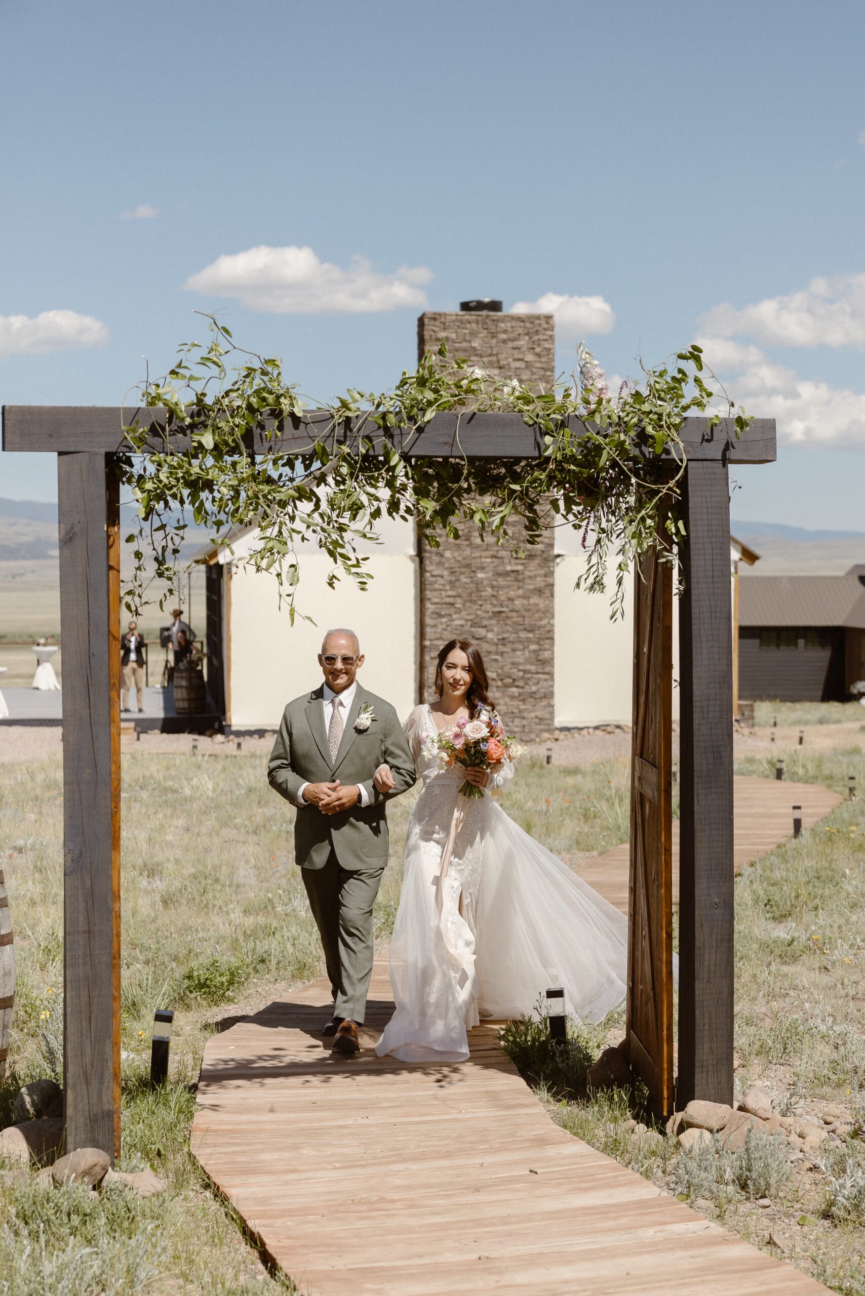 A bride and her father walk along a wooden path to the wedding ceremony location at Three Peaks Ranch. Photo by Colorado wedding photographer Ashley Joyce.
