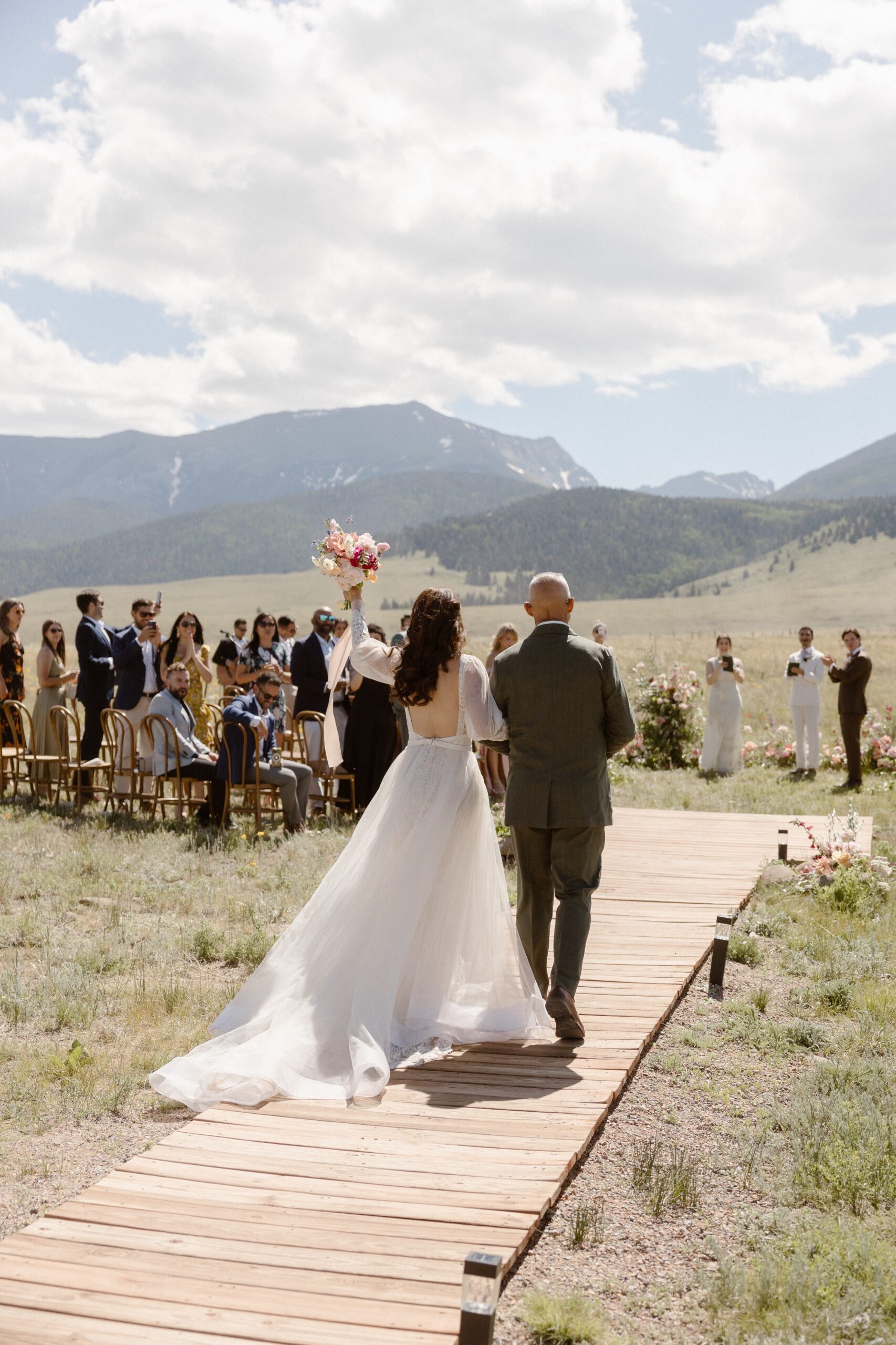 A bride and her father walk along a wooden path to the wedding ceremony location at Three Peaks Ranch. Photo by Colorado wedding photographer Ashley Joyce.