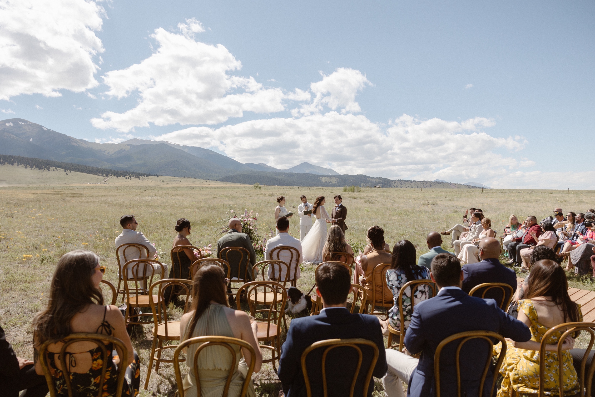 A wide view of a bride and groom standing in a grassy field with mountains in the background as they host their Three Peaks Ranch wedding. Photo by Colorado wedding photographer Ashley Joyce.