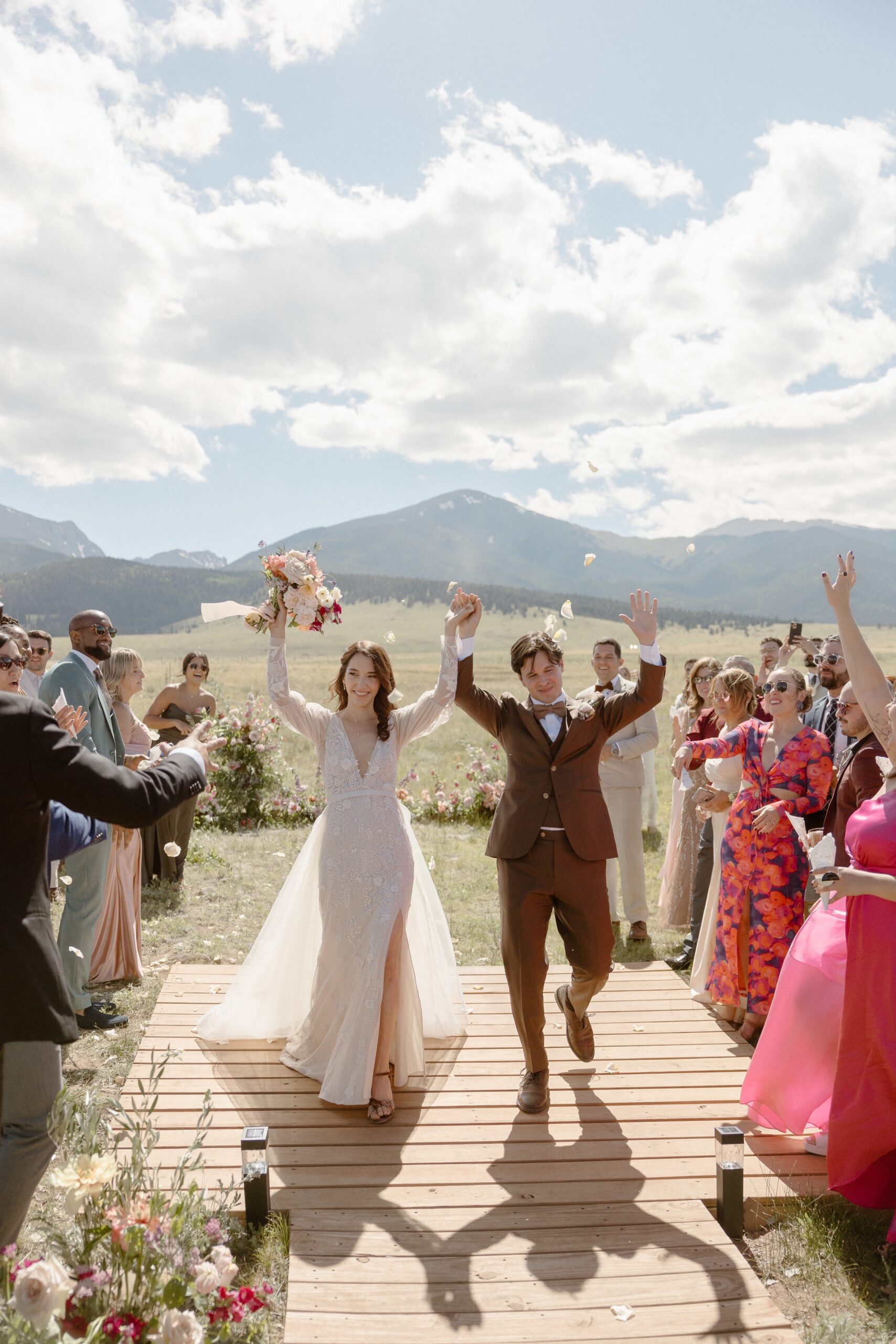 A bride and groom walk back down their wedding aisle as they celebrate their union while they raise their hands in the air. Photo by Colorado wedding photographer, Ashley Joyce.