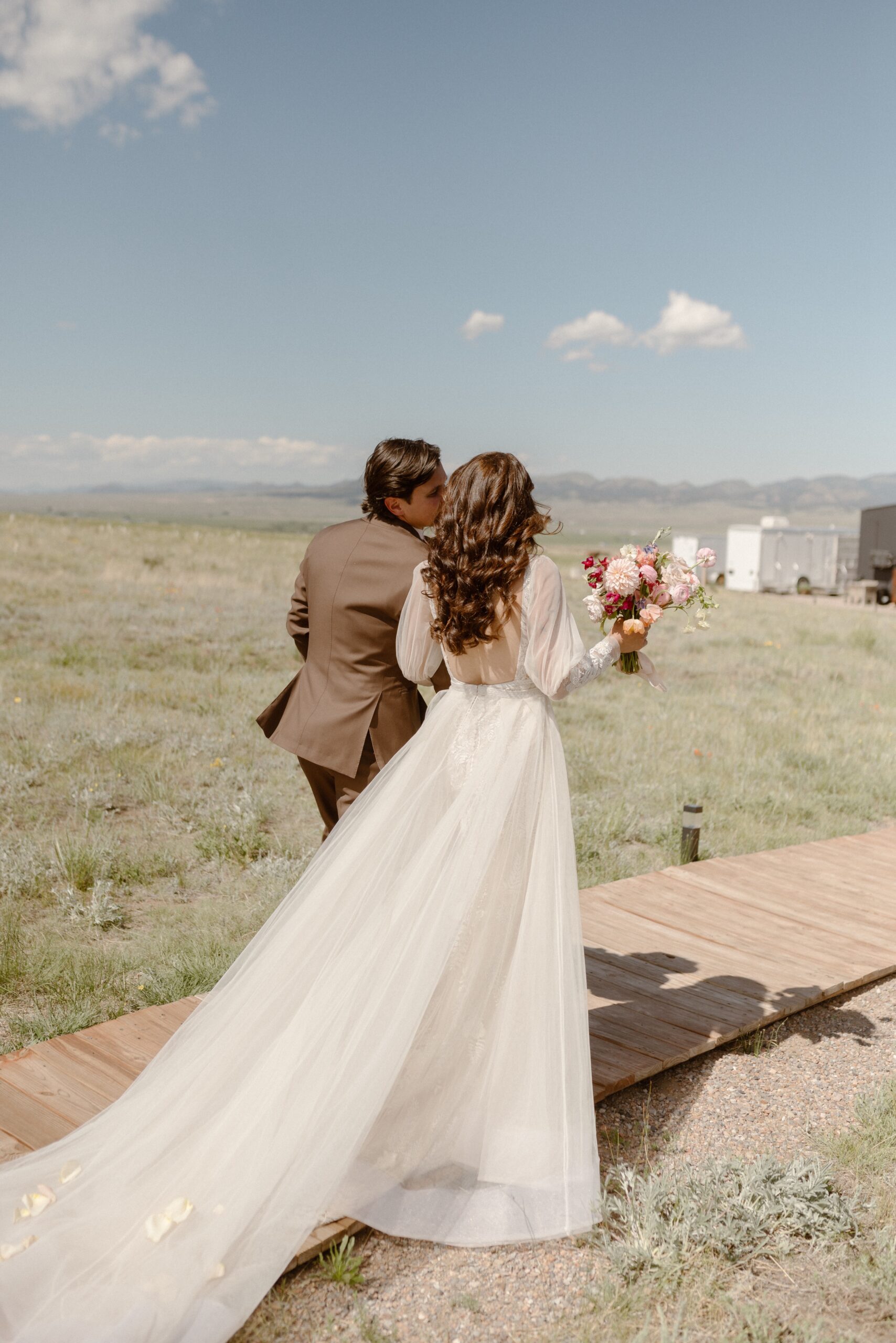 A bride and groom kiss each other on a wooden path in a grassy field at Three Peaks Ranch. Photo by Colorado wedding photographer Ashley Joyce.