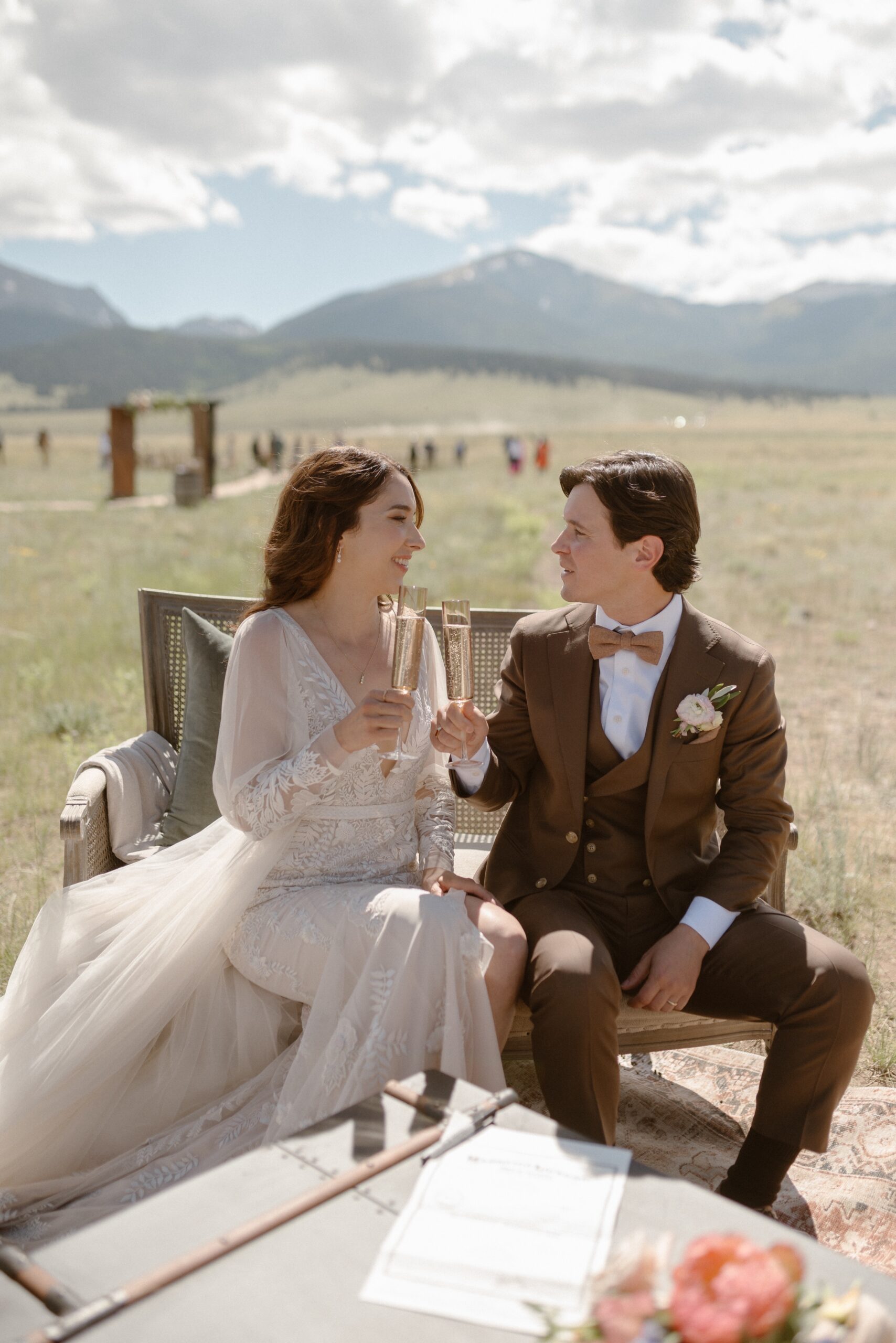 A married couple drinks champagne while sitting in a on lounge chairs in a grassy field at Three Peaks Ranch. Photo by Colorado wedding photographer Ashley Joyce.