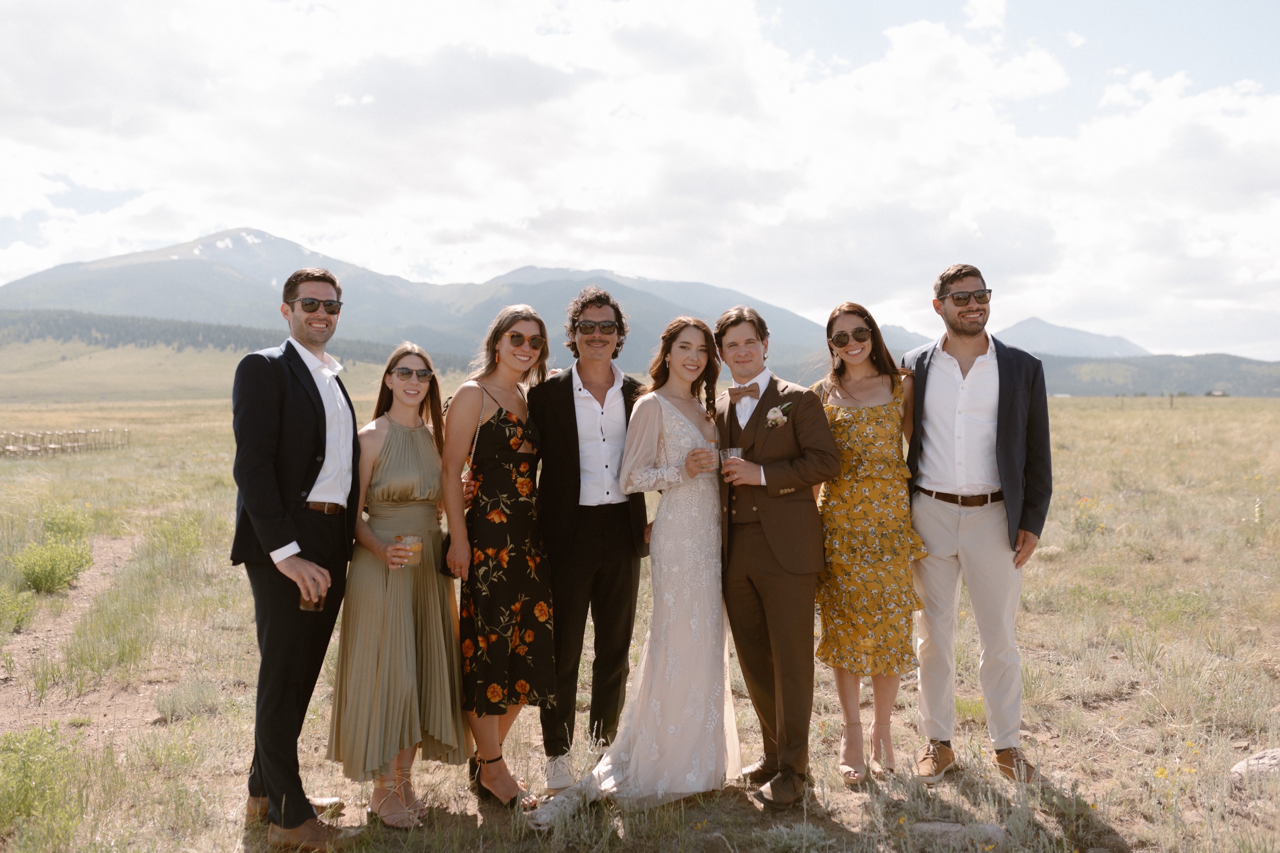 Six wedding guests pose with the bride and groom in a grassy field for a wedding portrait at Three Peaks Ranch. Photo by Colorado wedding photographer Ashley Joyce.