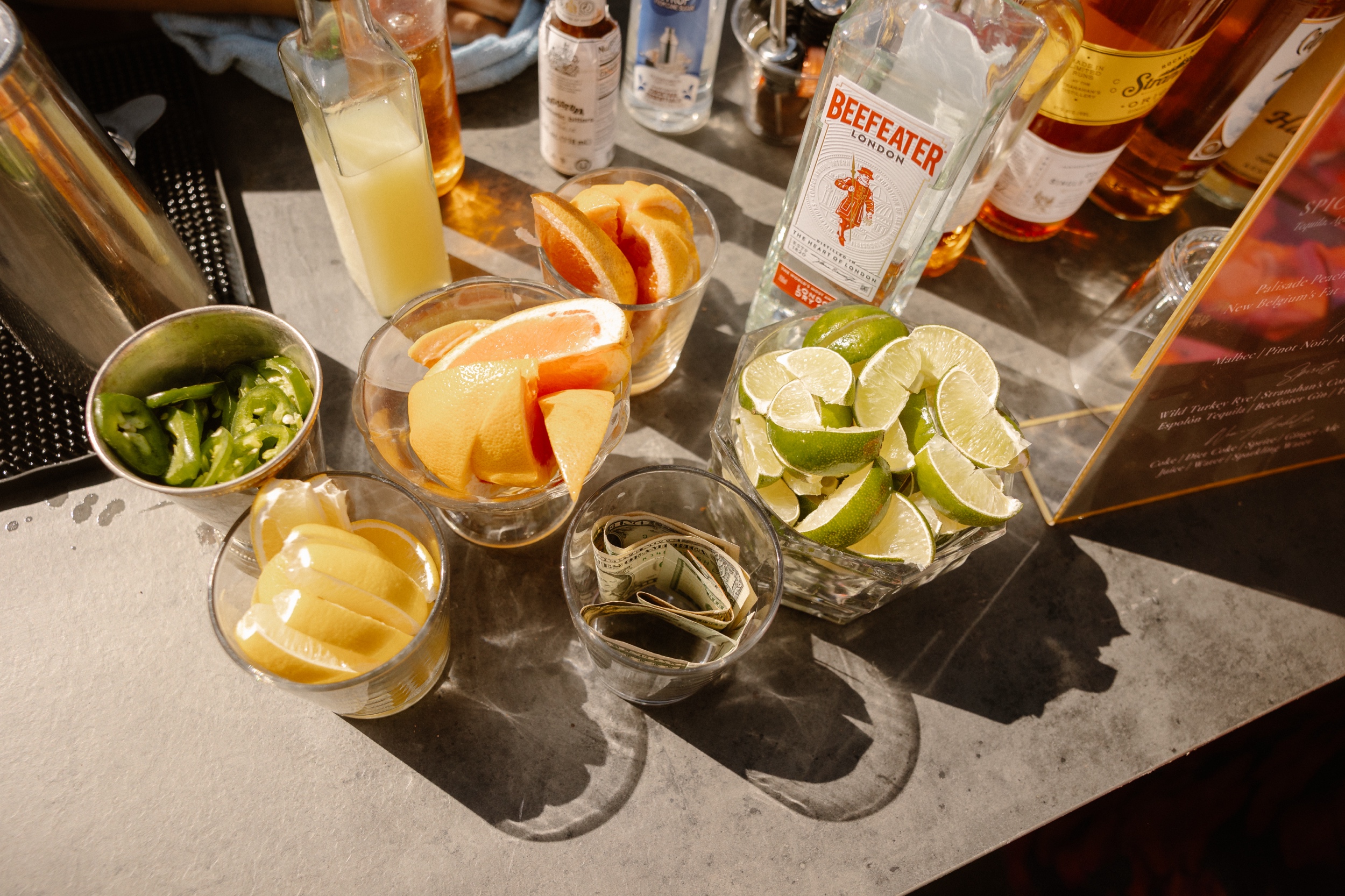 Cups of citrus, jalapenos, and cash with bottles of liquor in the background, with a focus on Beefeater Gin. Photo by Colorado wedding photographer Ashley Joyce.
