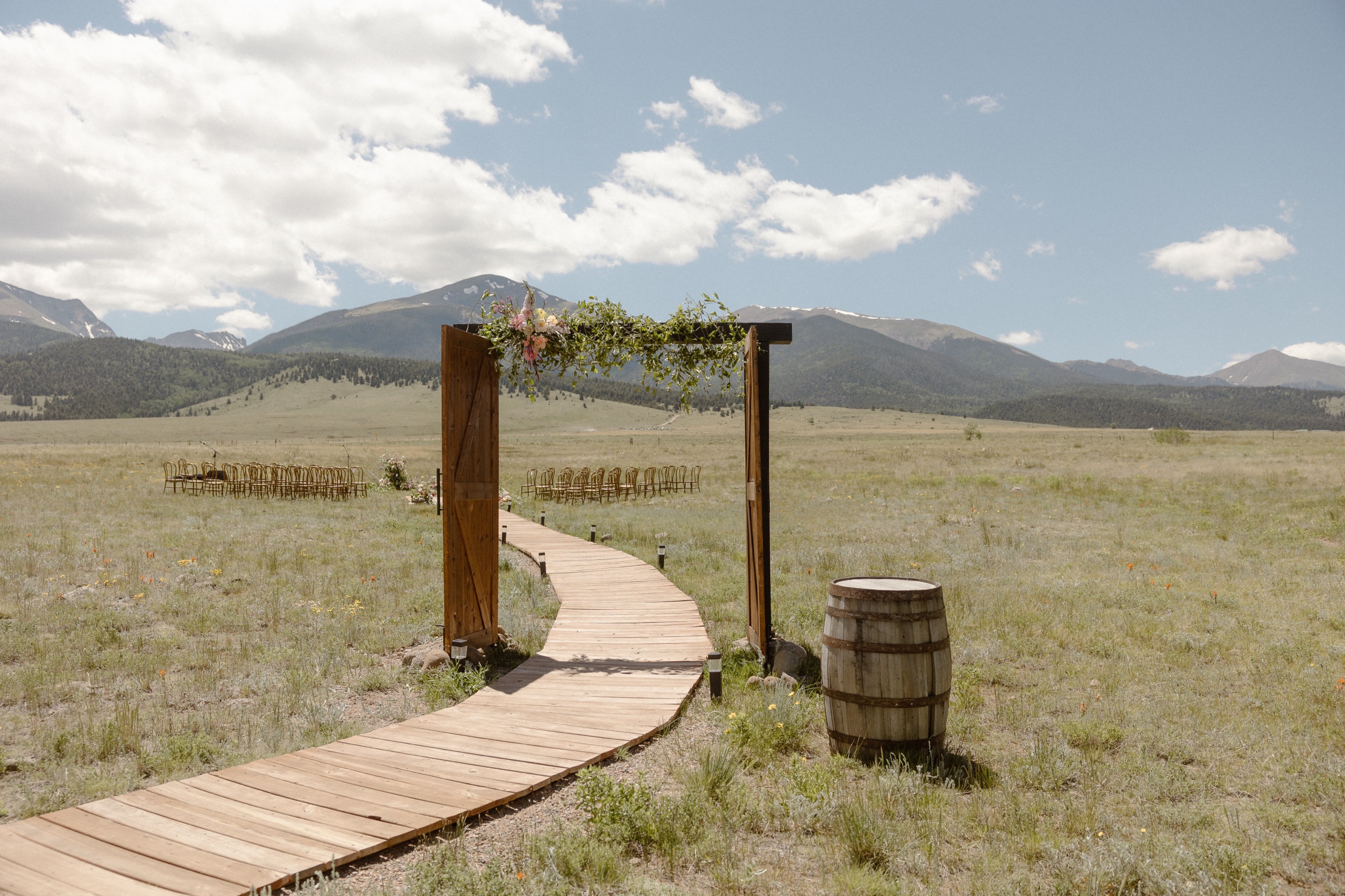 A photo of a wooden arch decorated in flowers and greenery with a minimal ceremony setup in the background for a Three Peaks Ranch wedding. Photo by Ashley Joyce.