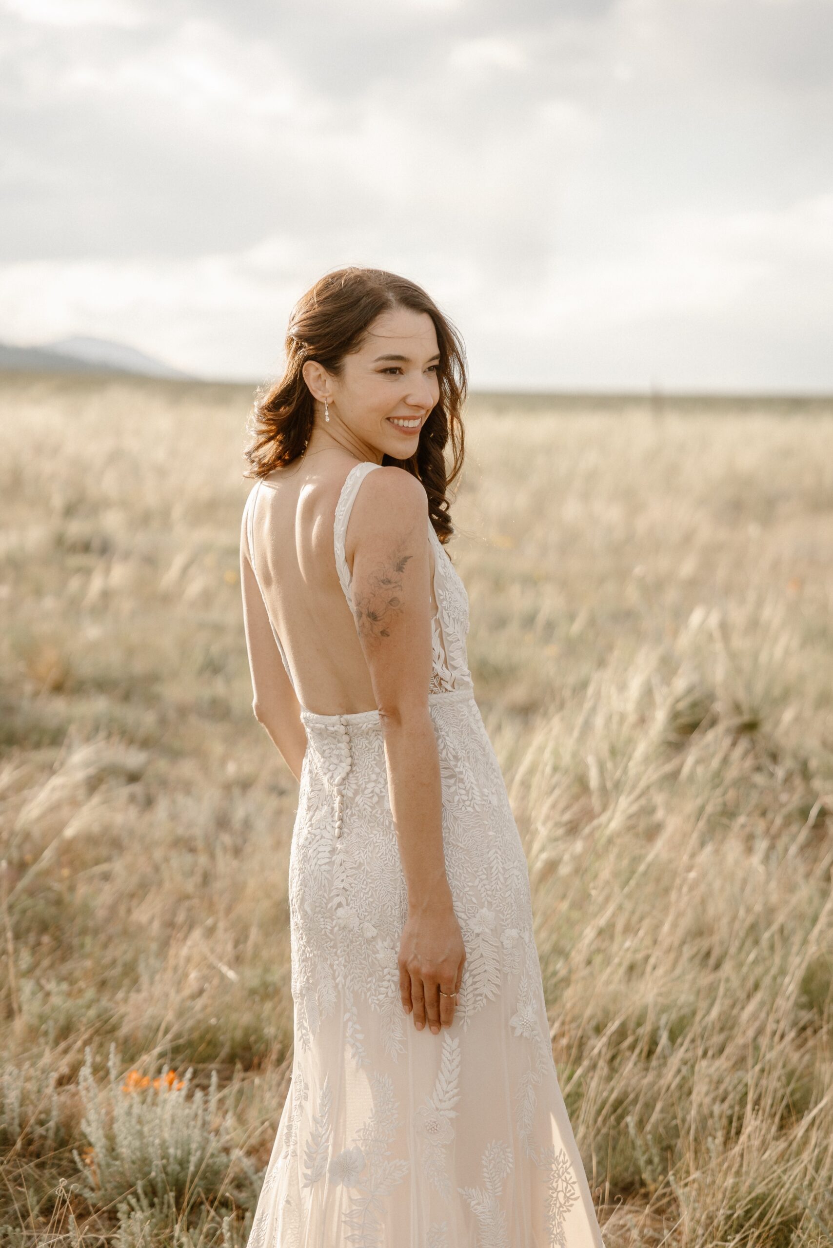A bride poses for her bridal portraits in a grassy field with the sun setting behind her. Photo by Ashley Joyce.