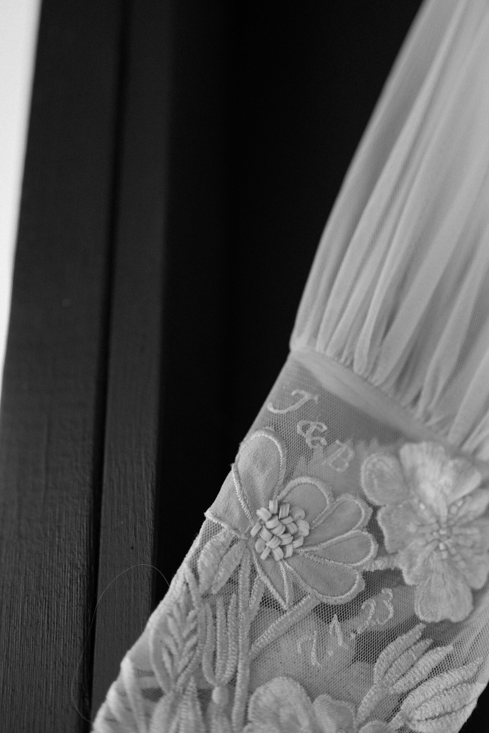 A black and white photo of the embroidery details of a bride's wedding dress. A black and white photo of wedding details for Jessica and Bernards wedding at Three Peaks Ranch. Photo by Ashley Joyce.