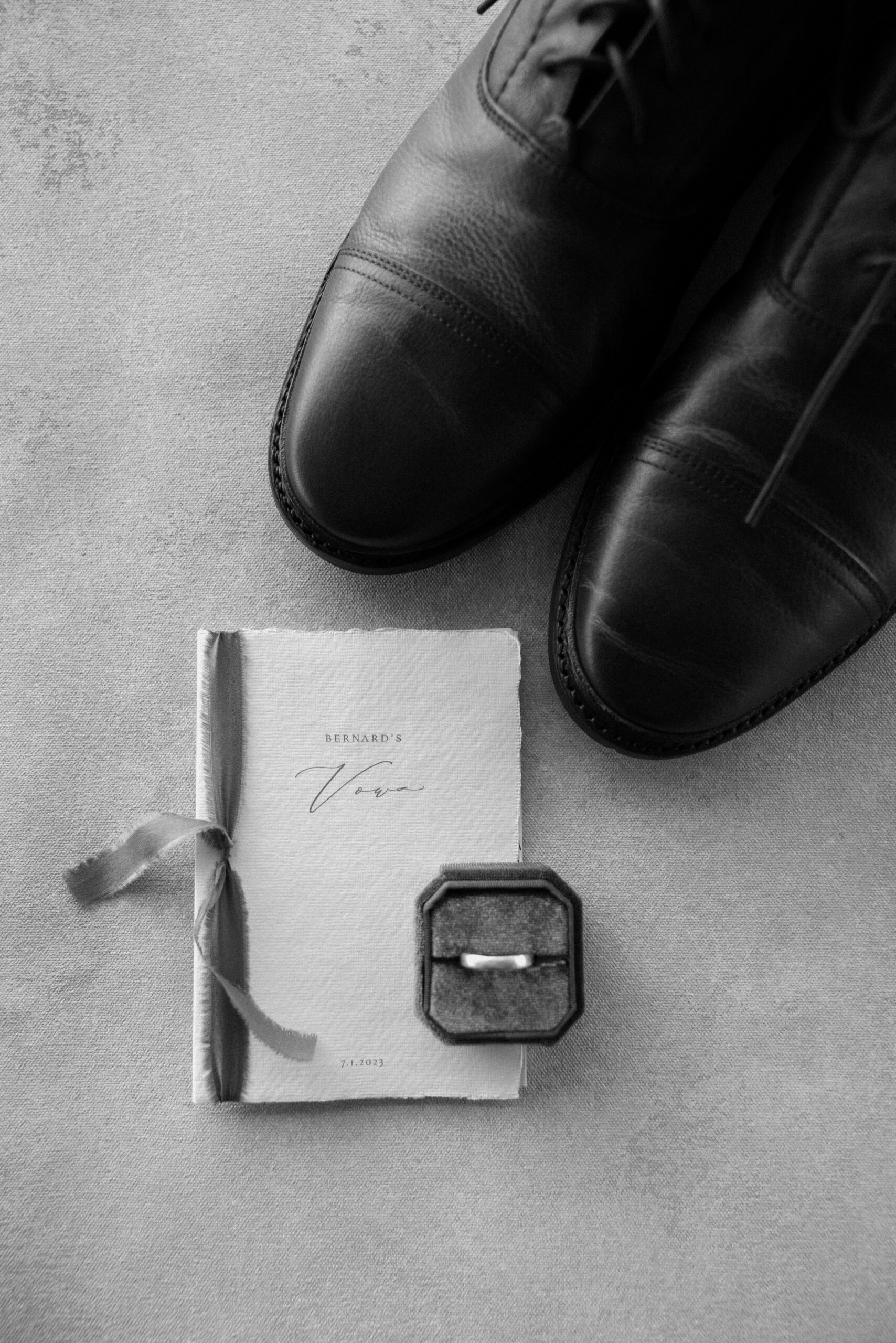 A black and white photo of a groom's vow book, wedding ring, and shoes. Photo by Ashley Joyce.