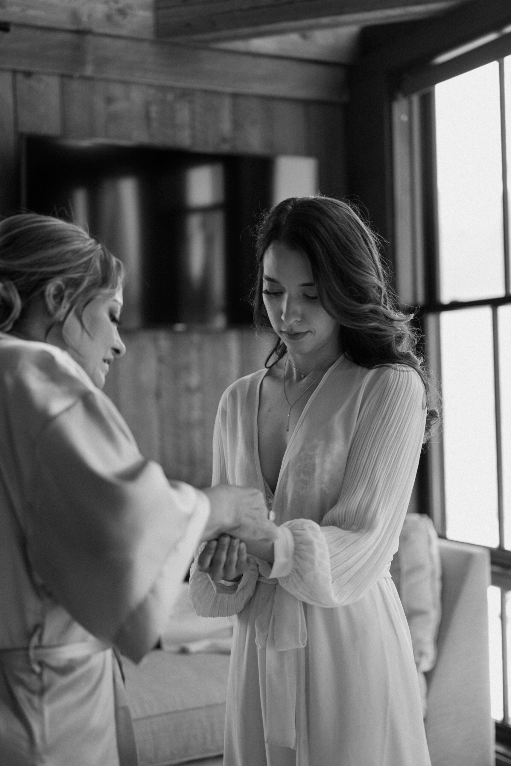 A bride holds her hand out to her mother while her mother puts jewelry on her wrist before her wedding at Three Peak Ranch. Photo by Ashley Joyce.