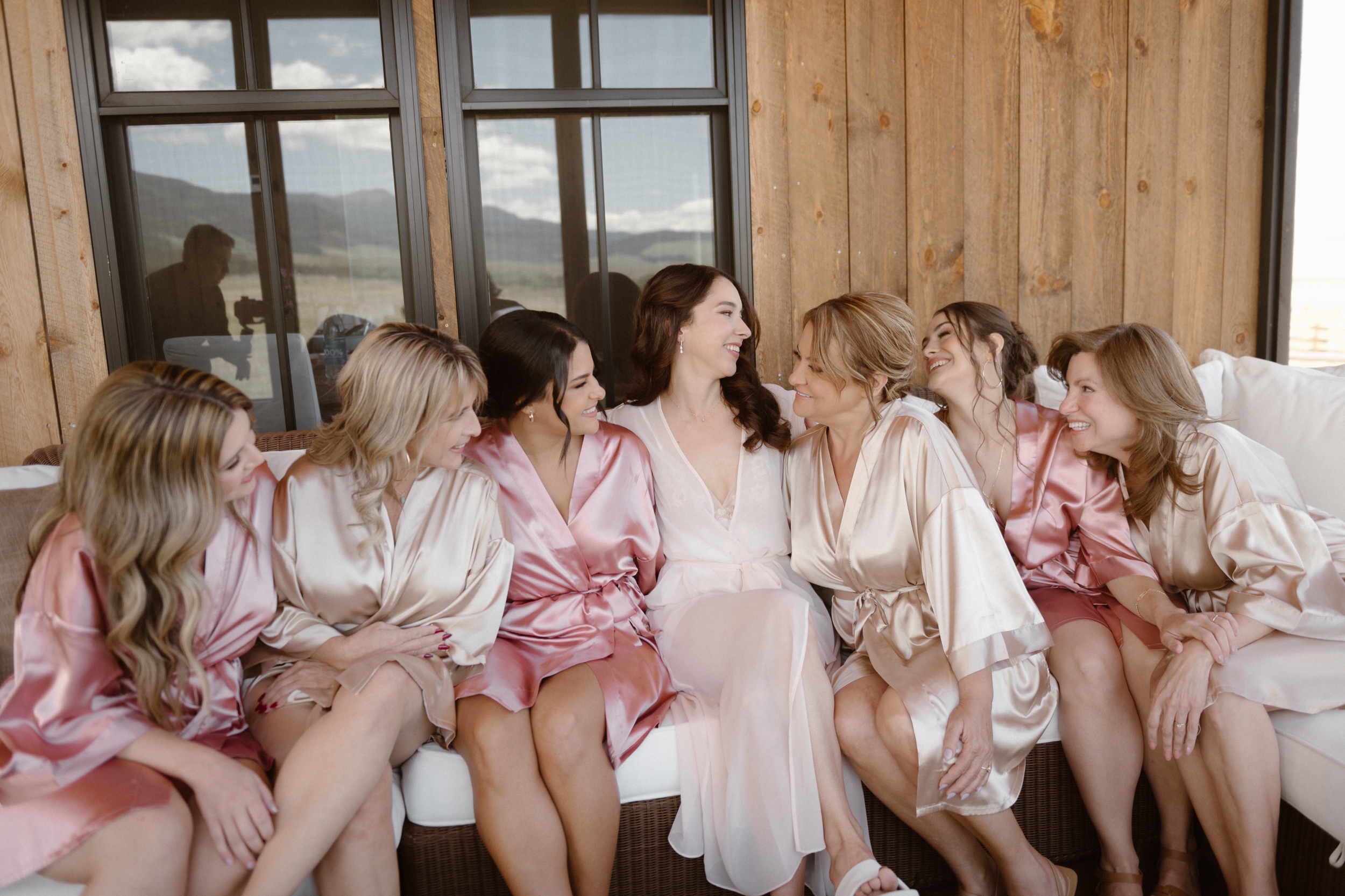 A bride and her bridesmaids and matronly family members sit in their satin robes at Three Peaks Ranch. Photo by Ashley Joyce.
