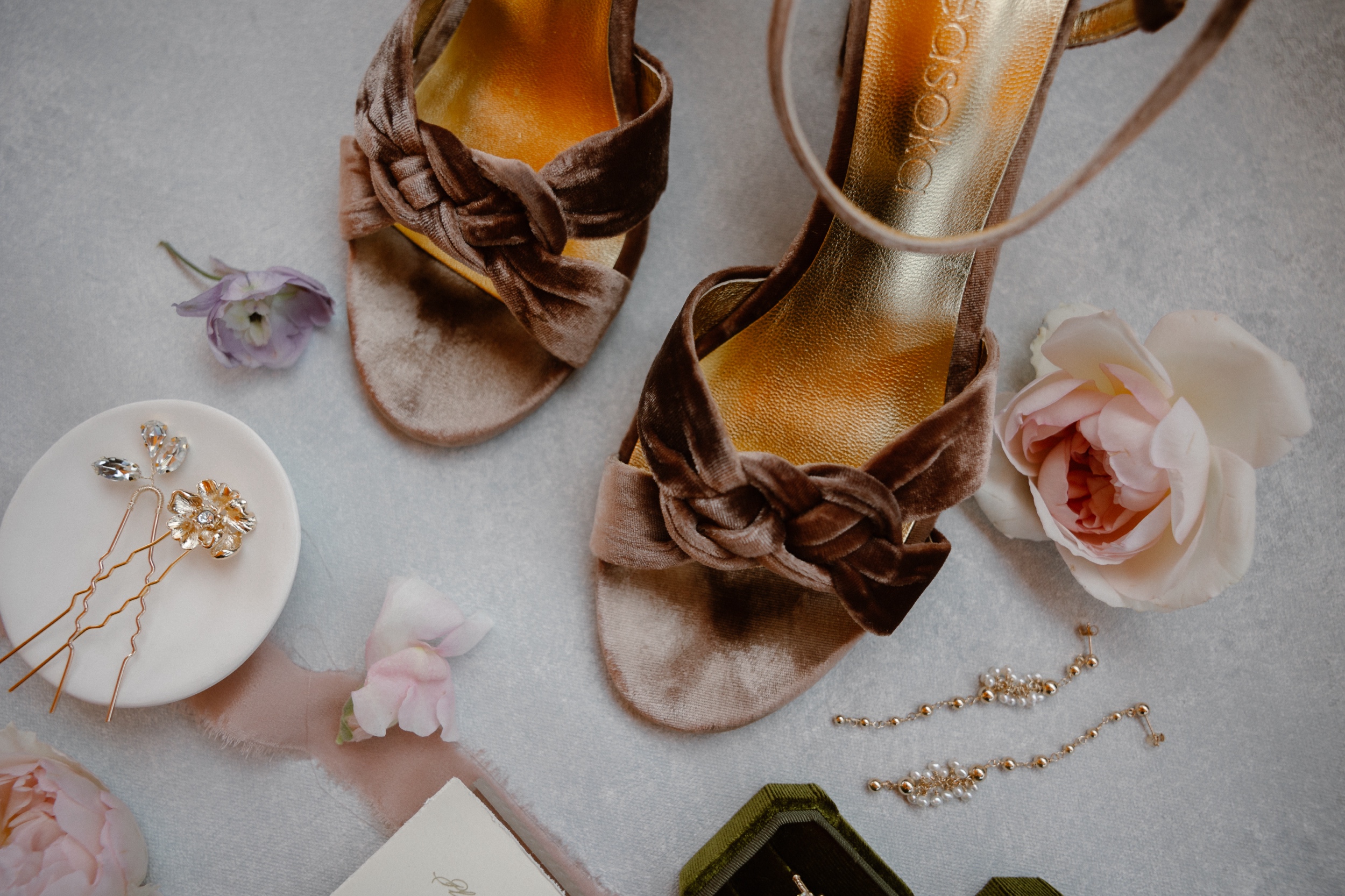 A color photo of a bride's wedding details, including her wedding shoes, hair pins, jewelry, and flowers. Photo by Ashley Joyce.