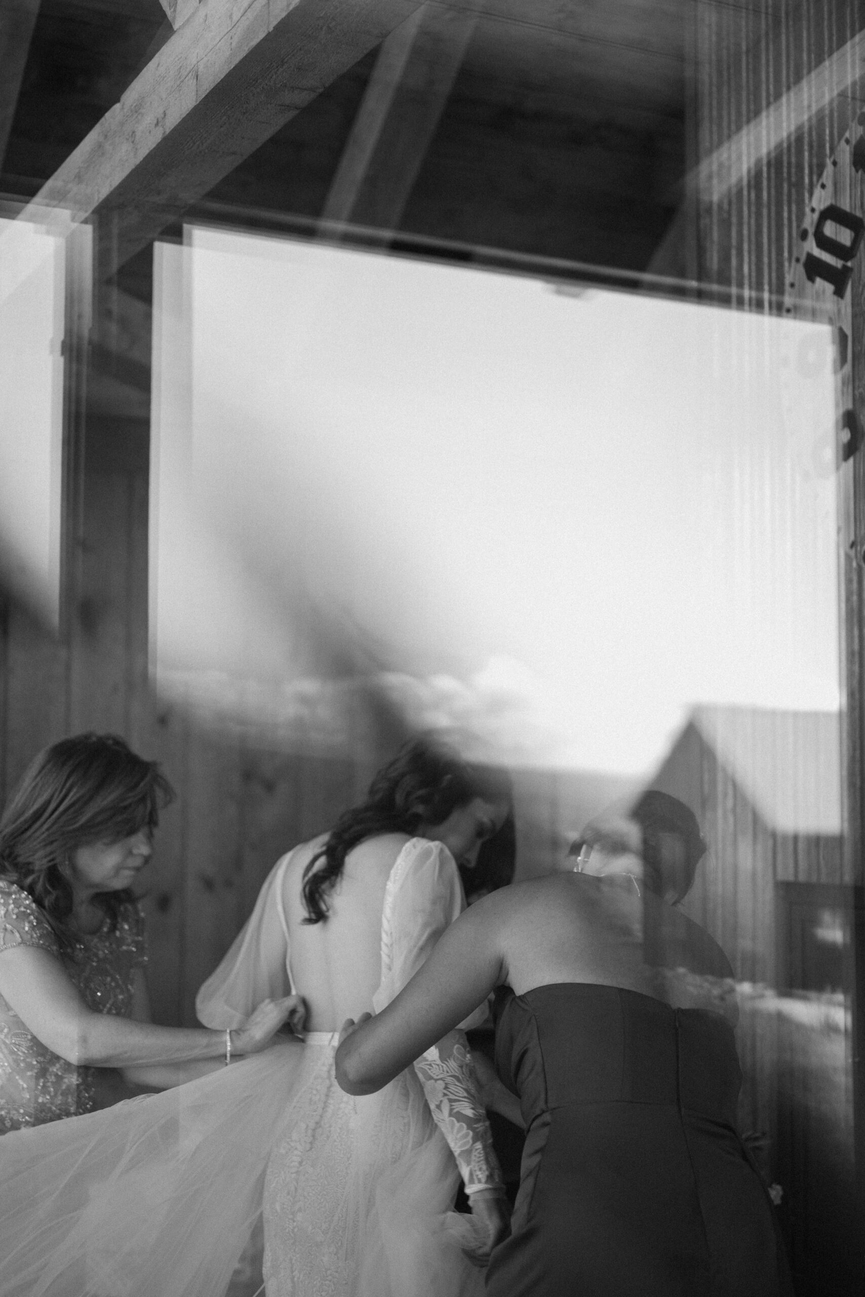 A black and white photo of a bride getting her wedding dress put on at Three Peaks Ranch. Photo by Ashley Joyce.
