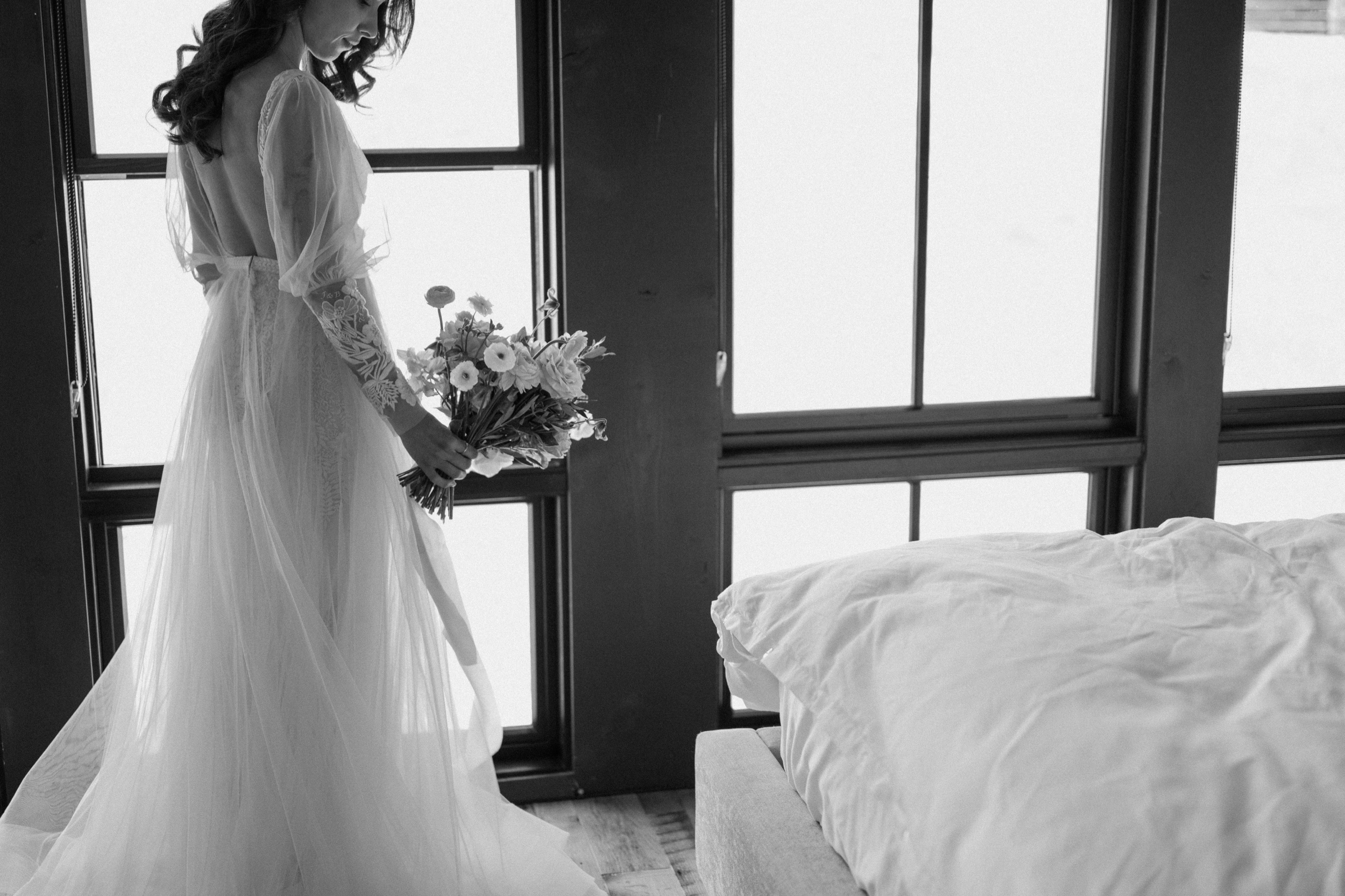 A black and white photo of a bride holding her wedding bouquet inside a cabin at Three Peaks Ranch. Photo by Ashley Joyce.