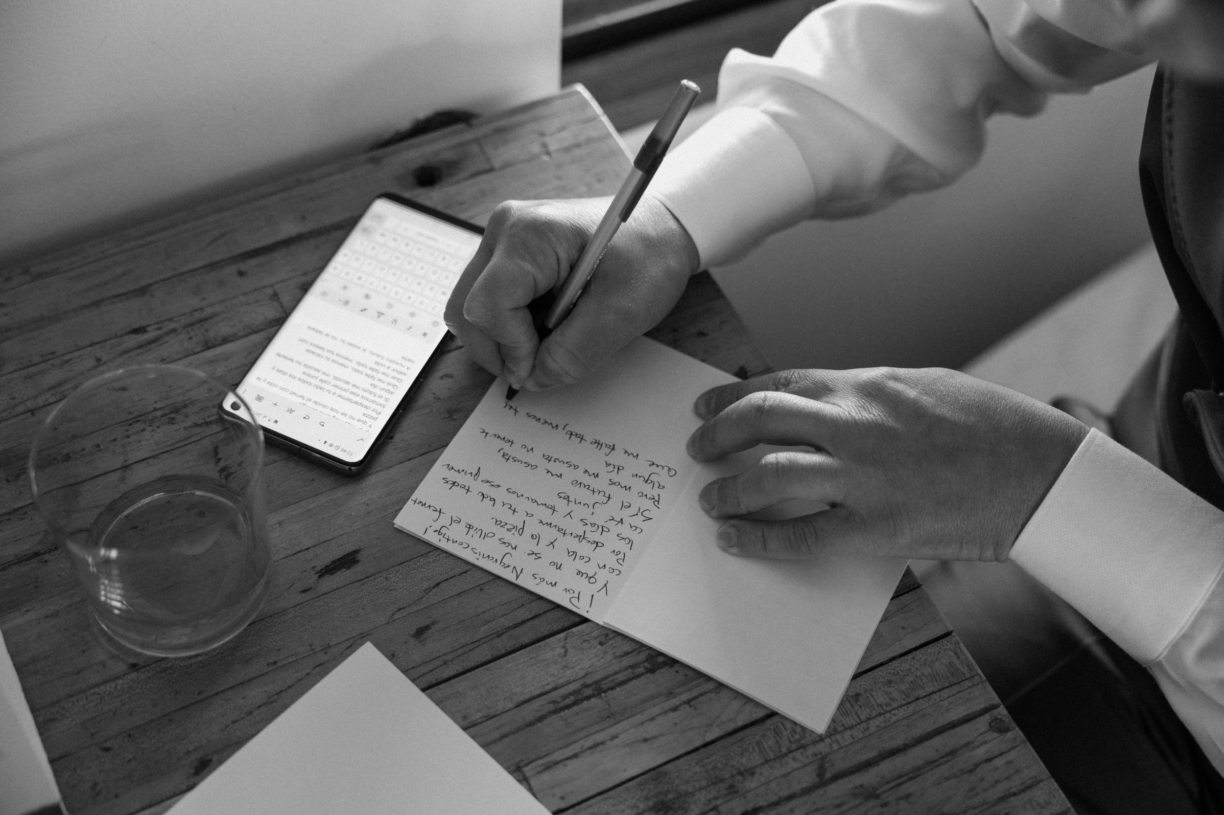 A black and white photo of a groom writing his vows in his vow book in Spanish as he prepares for his Three Peaks Ranch wedding. Photo by Colorado wedding photographer Ashley Joyce.